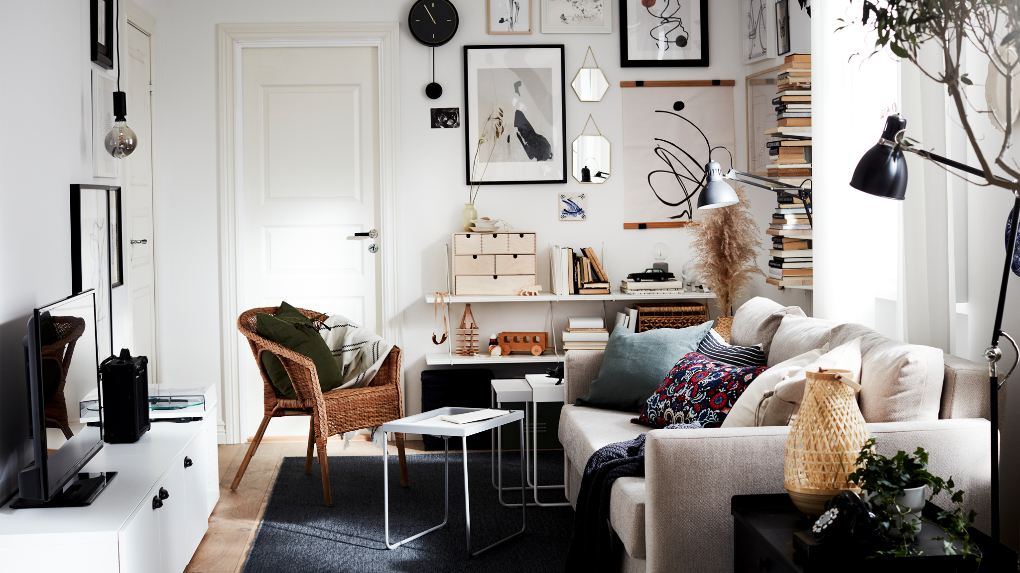 A small living room with a sofa, a TV bench, a vertical book display and an art wall, all in black, white and oatmeal.