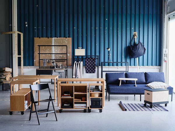 A variety of RÅVAROR furnishings including tables, a day-bed and storage units are set against a teal zinc plate wall.