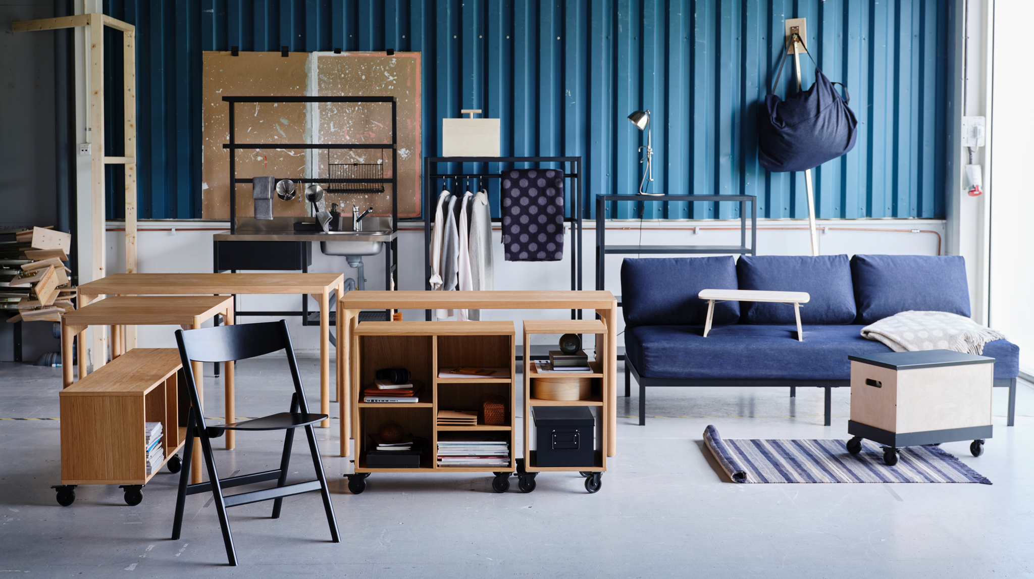 A variety of RÅVAROR furnishings including tables, a day-bed and storage units are set against a teal zinc plate wall.