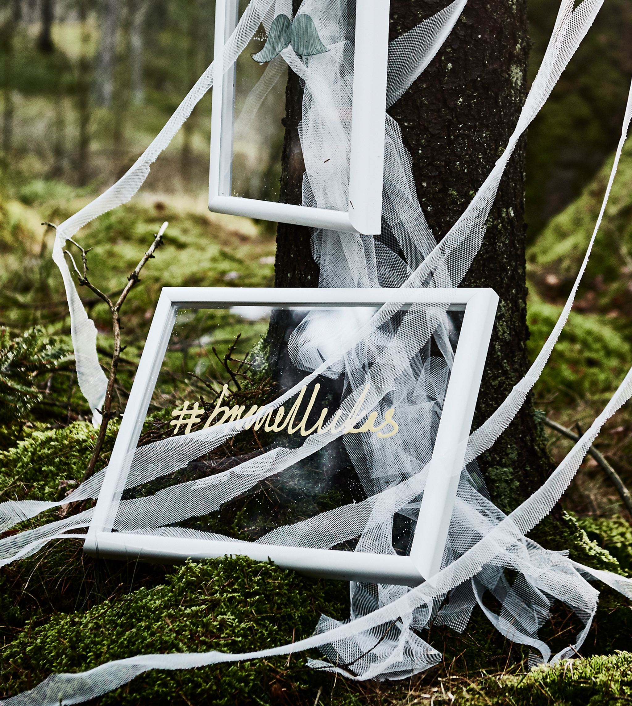 A wedding hashtag painted on the clear plastic glass of a frame for a DIY wedding photobooth