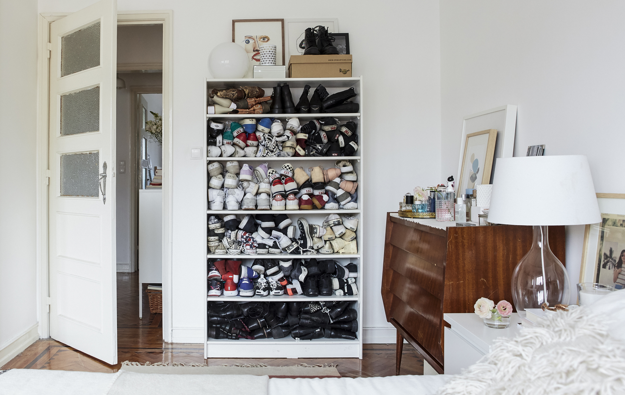 A white bedroom with wooden floors and shoes stacked in a bookcase.