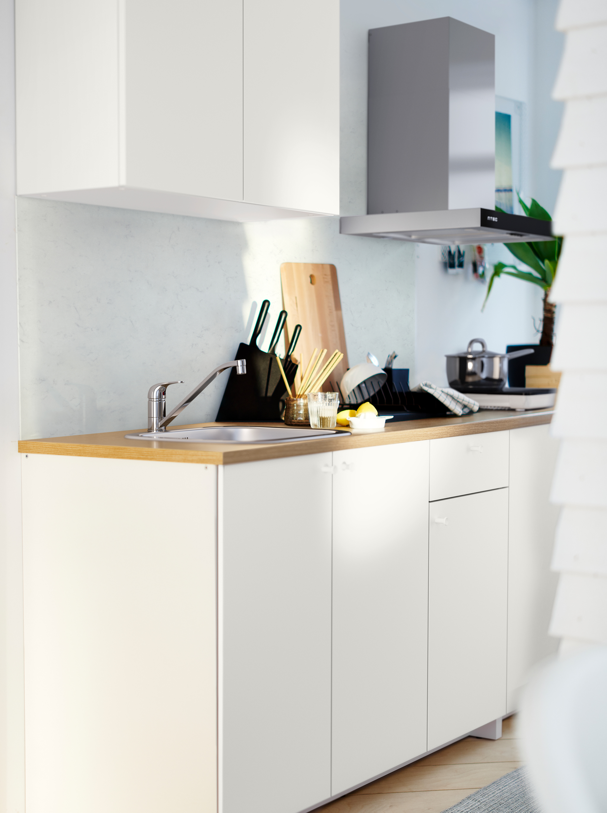 A white KNOXHULT kitchenette with a wooden worktop, potted herbs, pots, knives and various kitchen accessories.