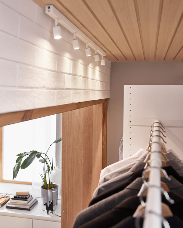 A white LED ceiling track is ceiling-mounted above a wardrobe solution, and the adjustable spotlights illuminate the clothes.