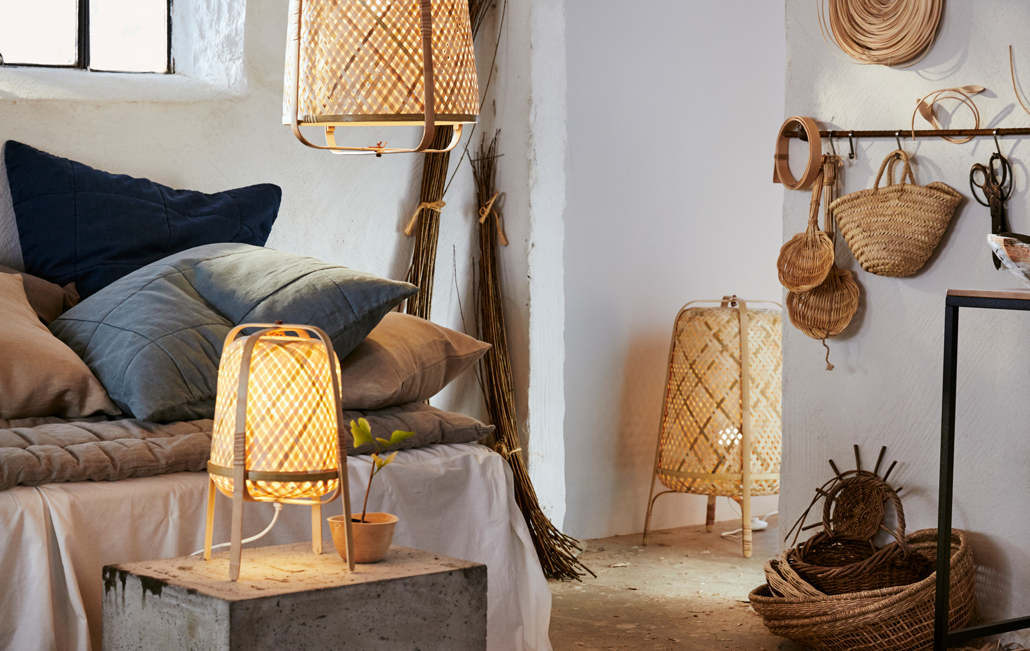 A white room with neutral textiles, rattan baskets, and a bamboo floor lamp, table lamp and pendant lamp.