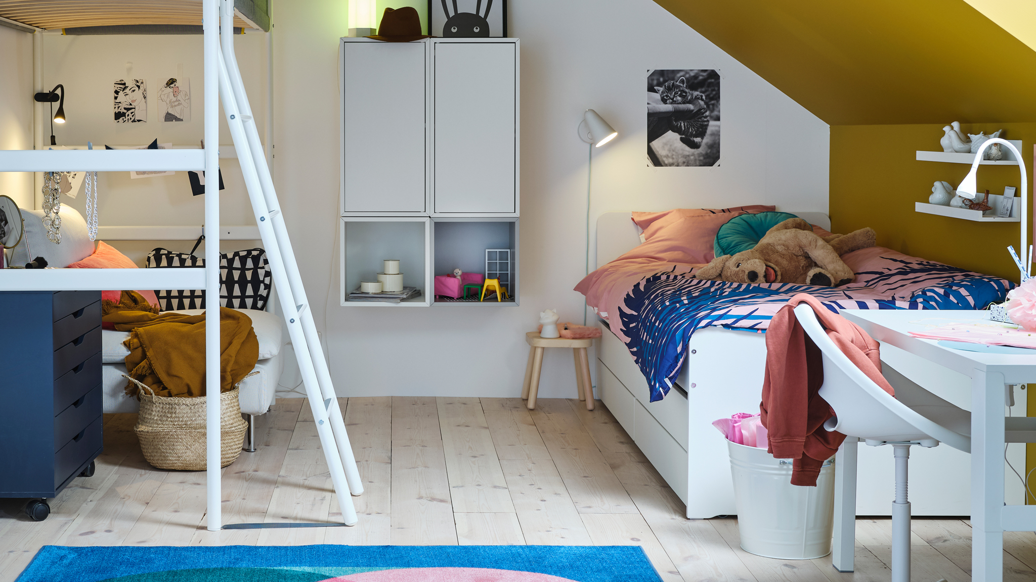 A white VITVAL loft bed stands opposite a white SLÄKT bed with underbed and storage in a children’s bedroom.