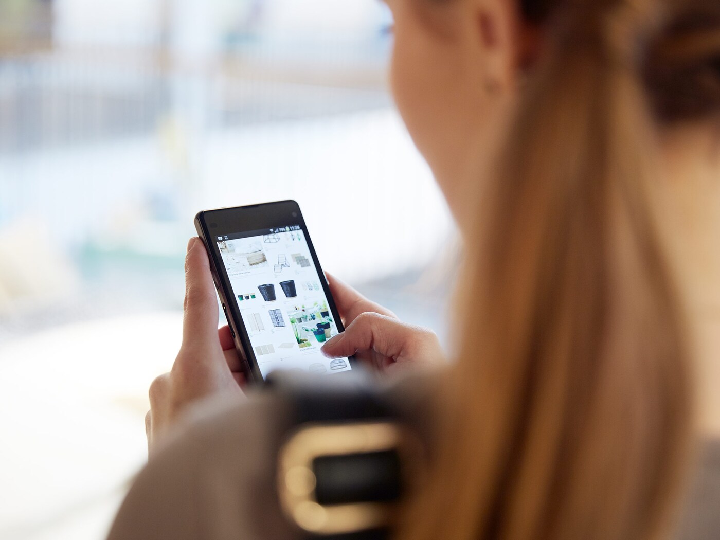 A woman holding a mobile telephone, while she browses a menu on the screen.