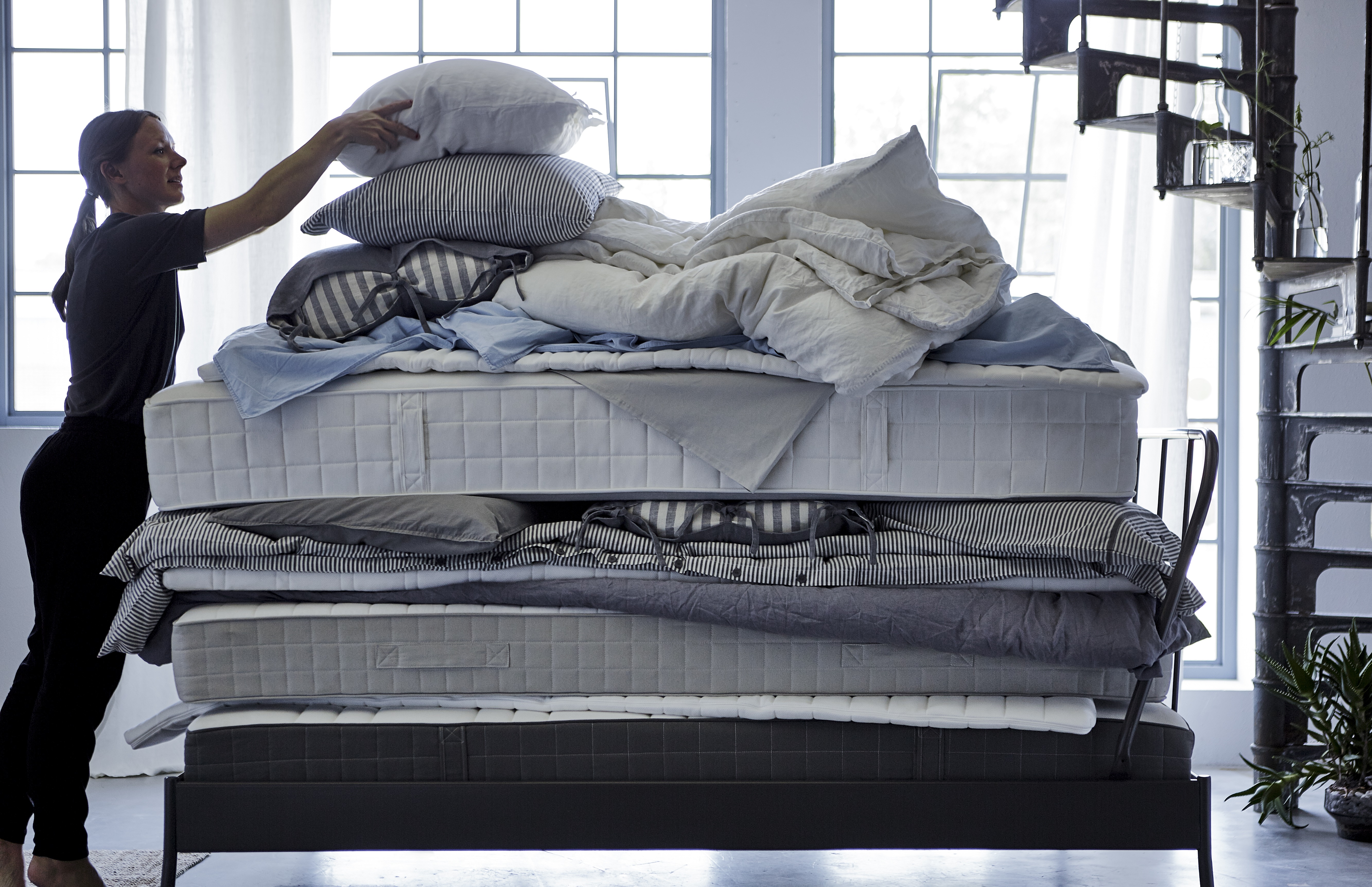 A woman putting a pillow on top of a stack of soft mattresses, quilts and bed textiles.