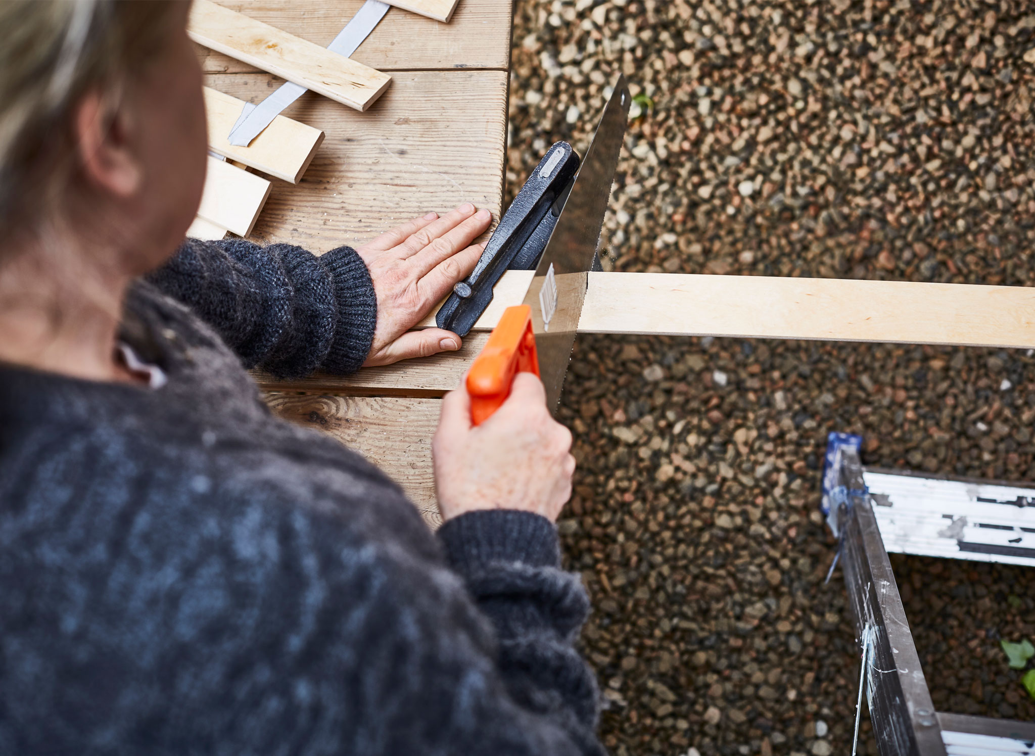 A woman saws bed slats to create a custom DIY trellis.
