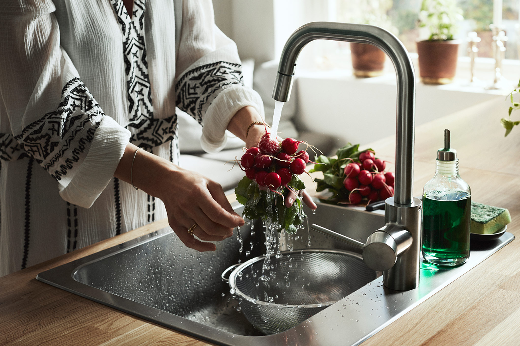 A woman standing by the sink rinsing a bunch of radishes using the ÄLMAREN kitchen tap.