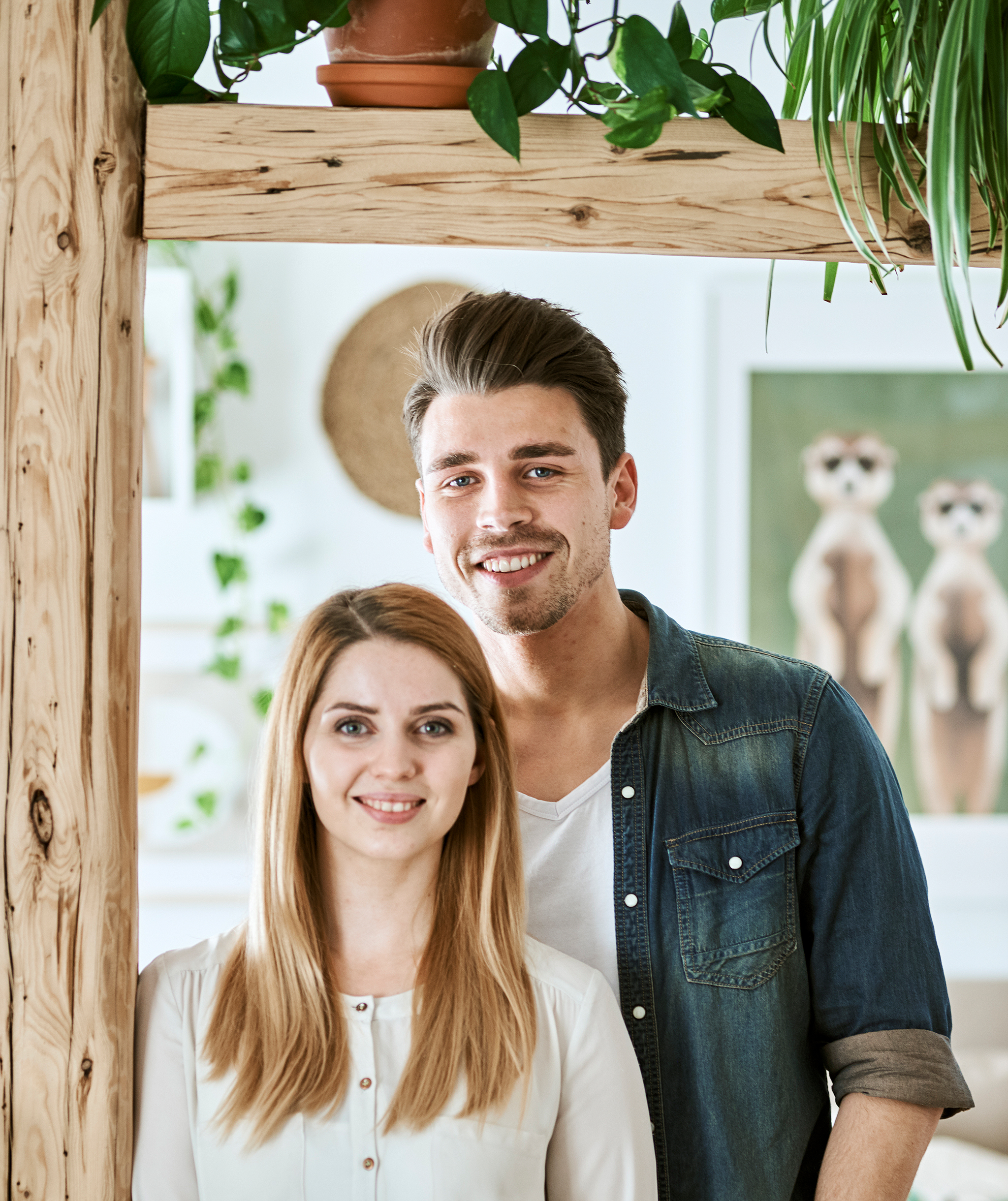 A young couple stand next to wood beams with framed illustrations on the wall behind them.