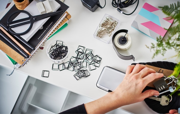 An aerial view of someone organising piles of tape, paper, paper clips, safety pins, keys and more to put in a drawer.