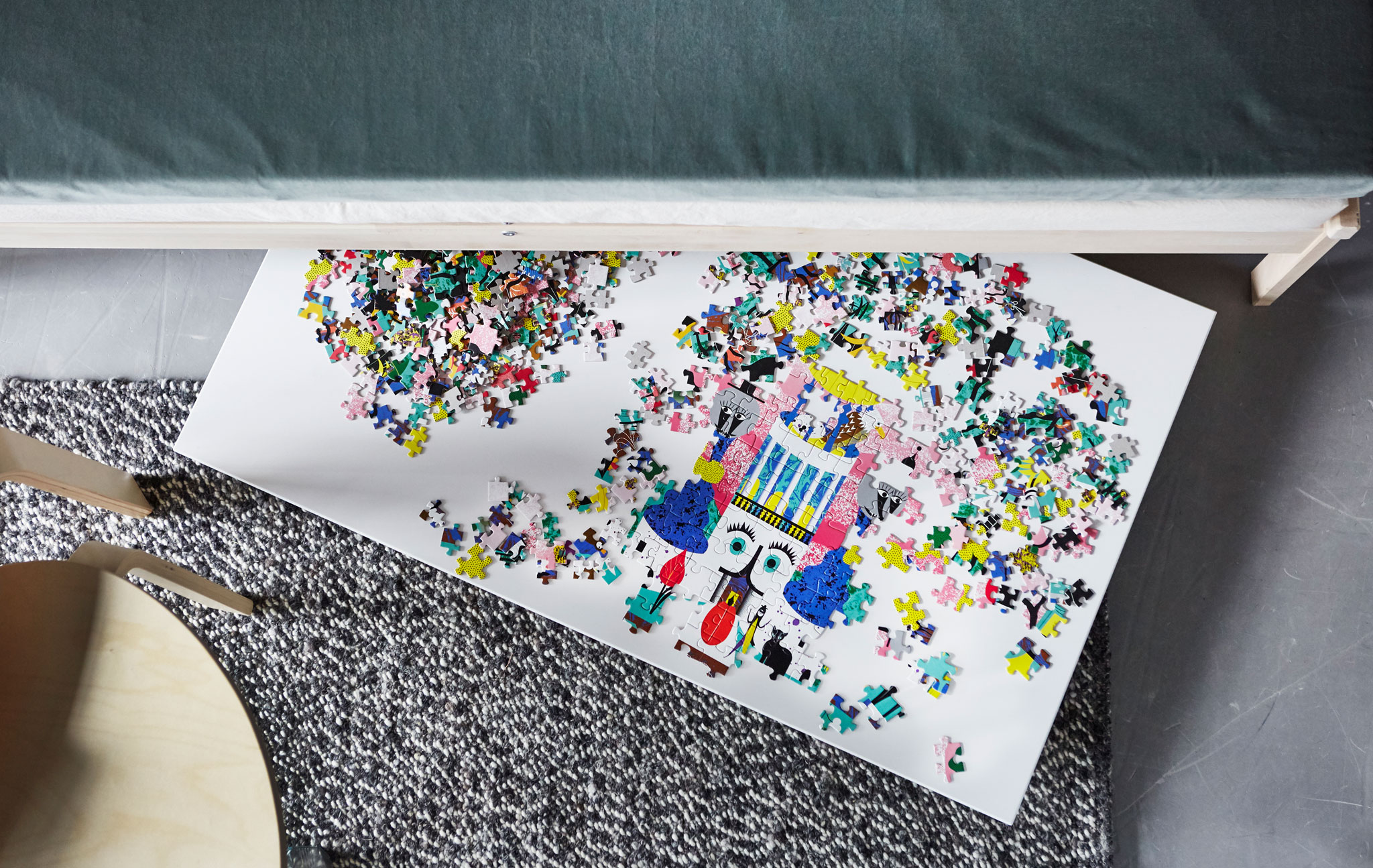 An overhead view of a puzzle on a board that’s sticking out from under a sofa.