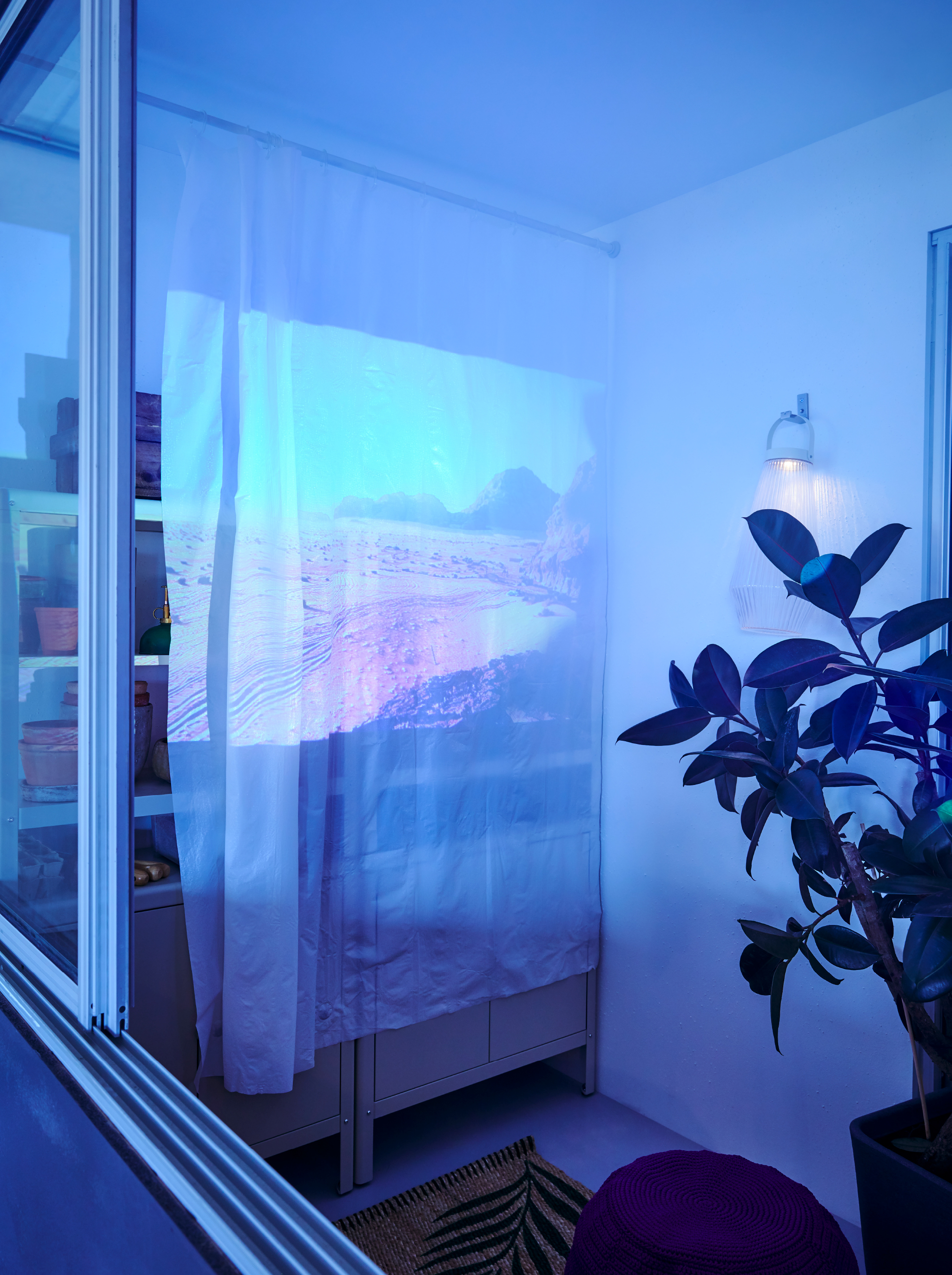 At one end of a balcony, a film is projected on a white BJÄRSEN shower curtain hung as a film screen from a BOTAREN rod.