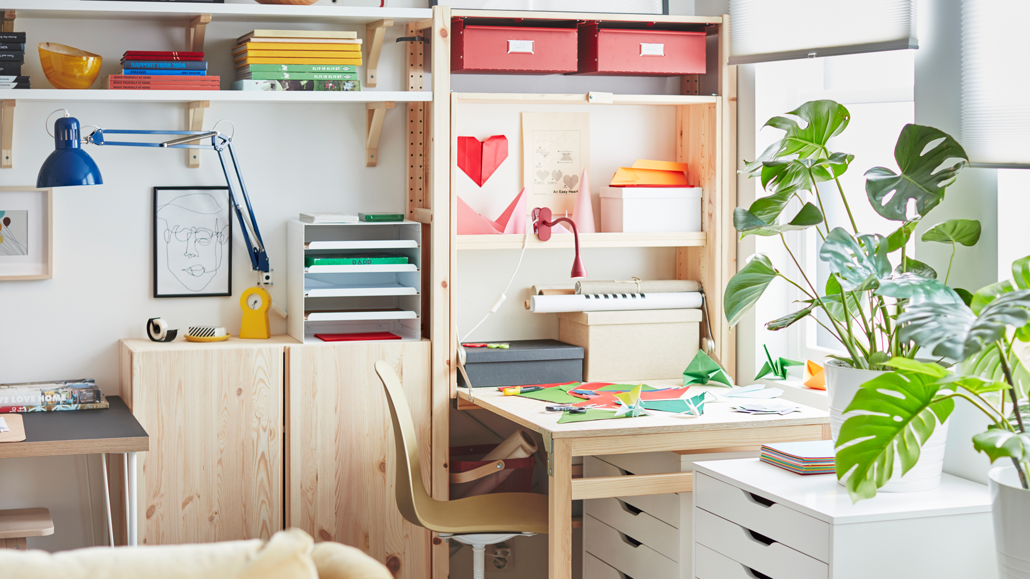 At one end of a wall-wide IVAR storage unit, a workspace created by a folded-out table, covered with coloured paper.