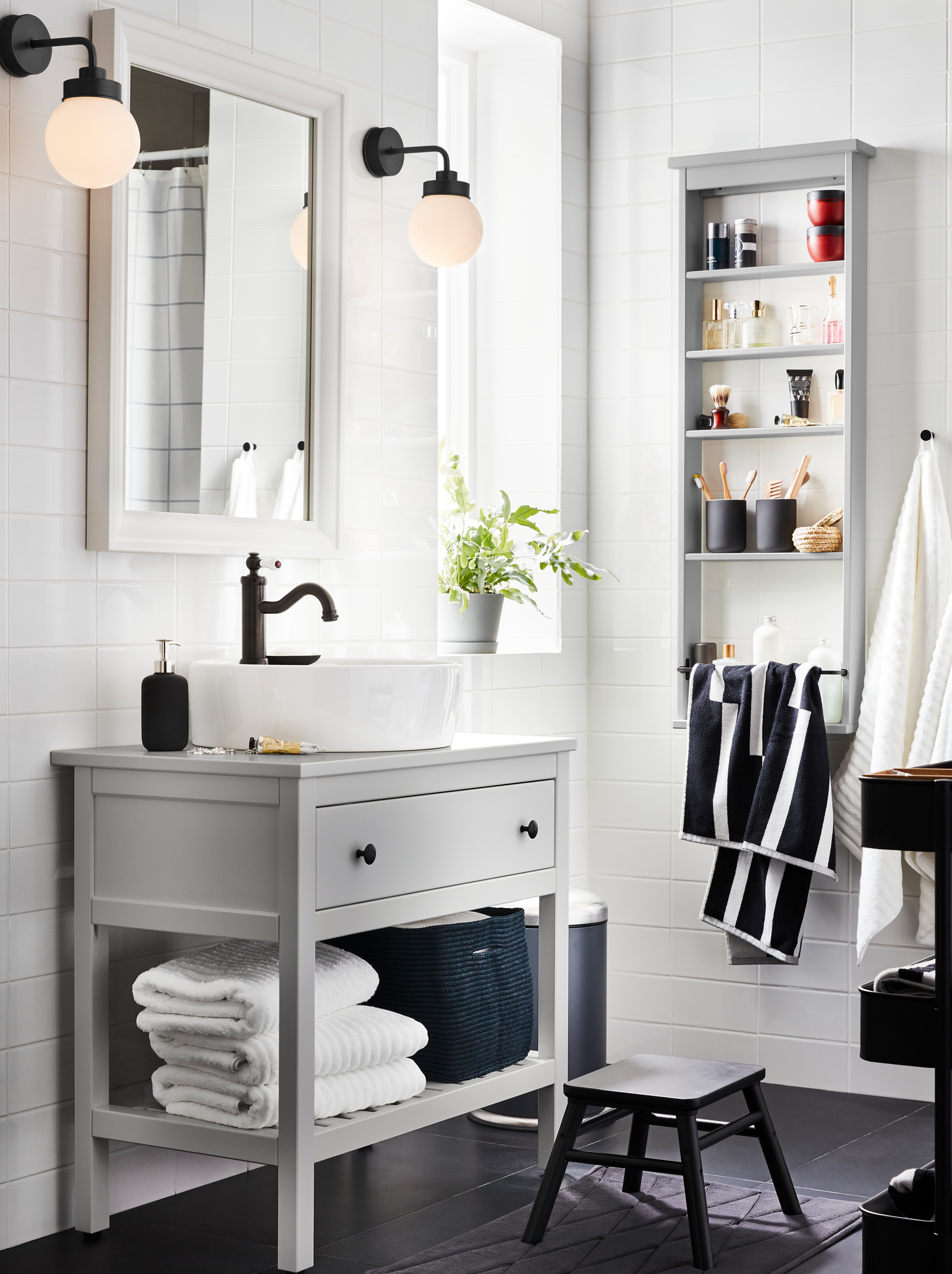 Bathroom with grey HEMNES one-drawer washstand, HEMNES wall shelf with towels, a HAMNSKÄR mixer, a mirror, and two lamps.