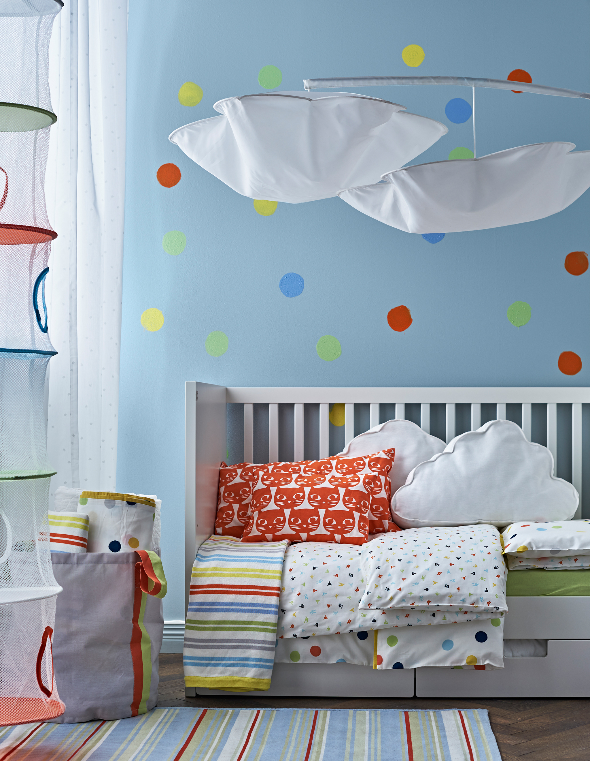 Bed textiles, a rug and a polka dot painted wall in primary and secondary colours that make it easy to go from a nursery to child’s room