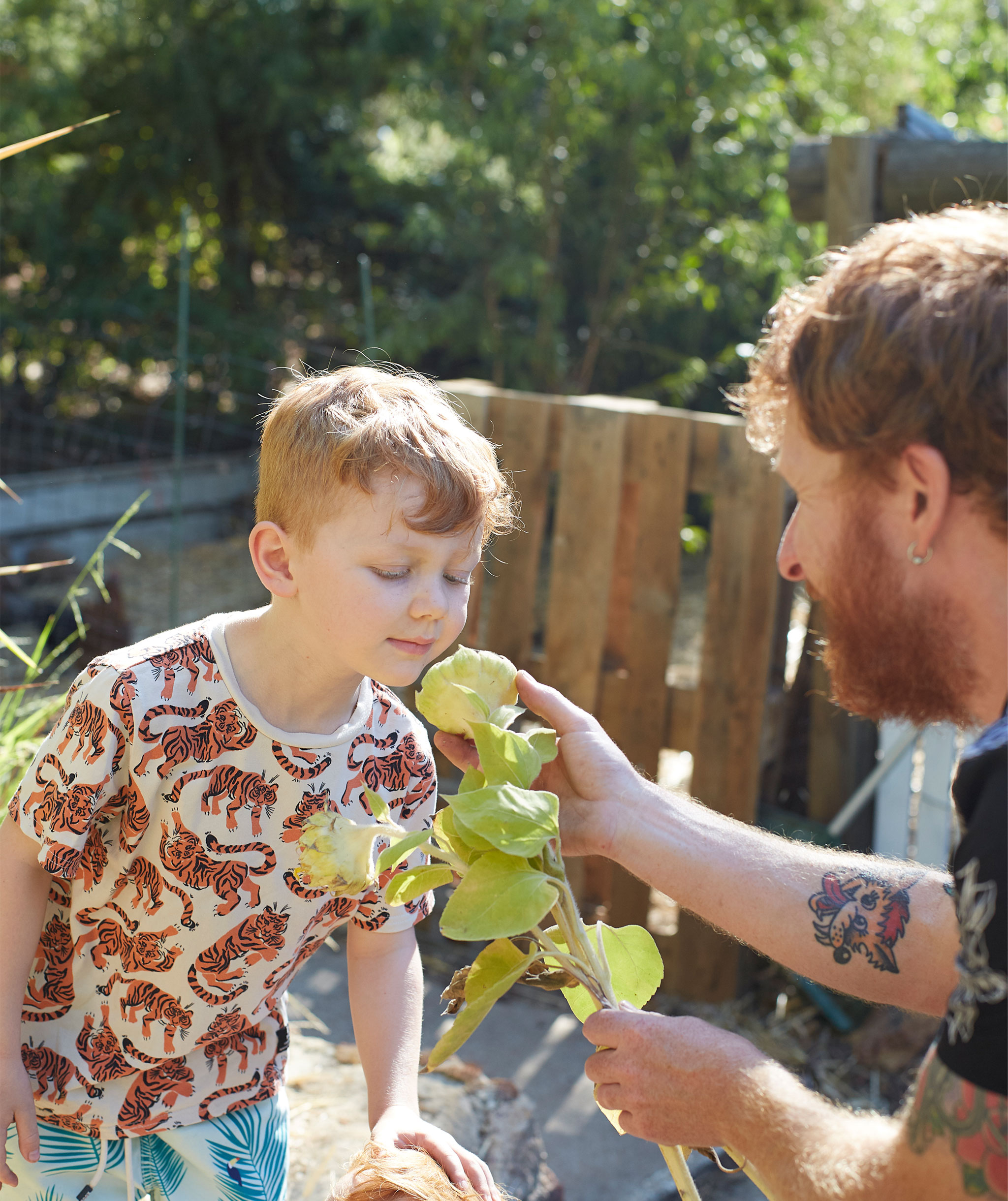 Ben helps his son smell a flower in the garden.