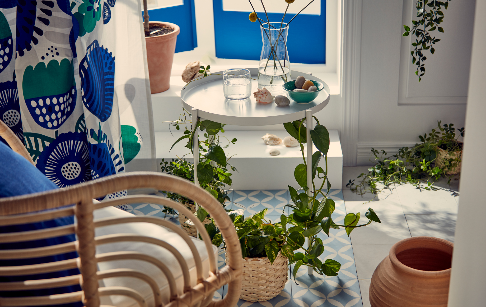 Blues and whites in a sunny spot just inside French balcony-style windows. Wicker armchair beside a plant-wrapped tray table.