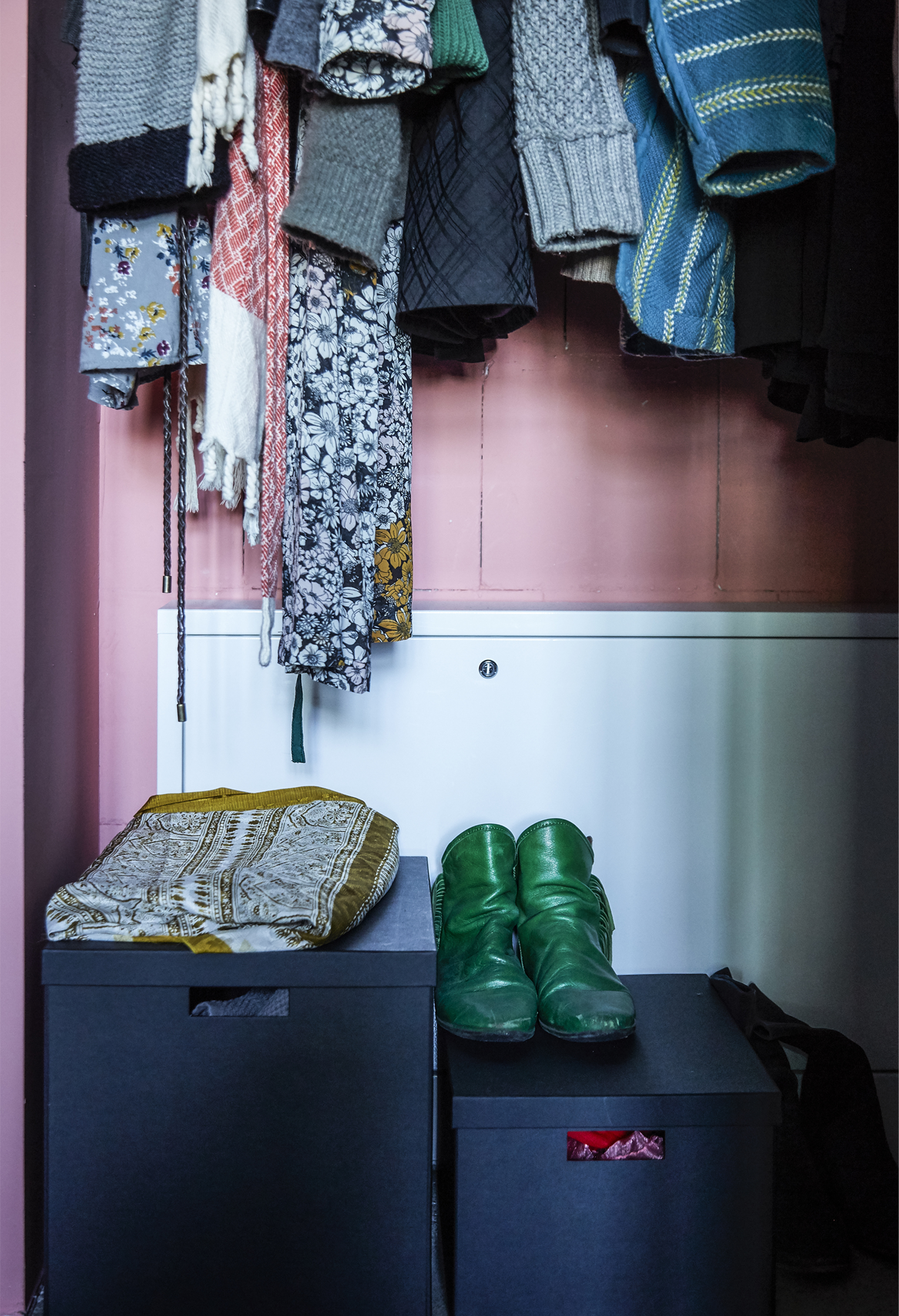 Coats hanging up with shoe boxes below.