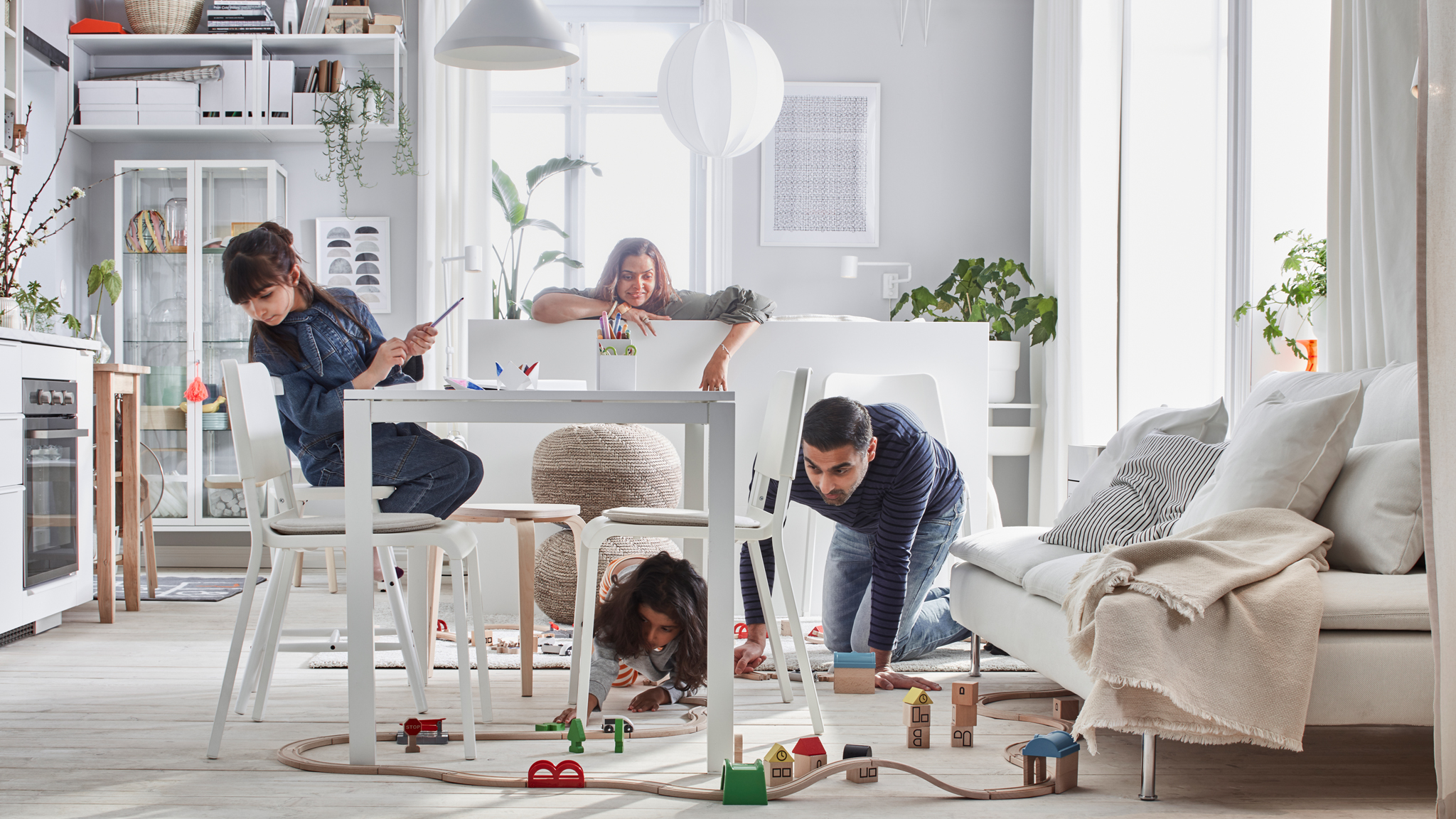 Compact-living home where a family plays with a LILLABO train set in a room with bed, sofa, table, kitchenette, and storage.