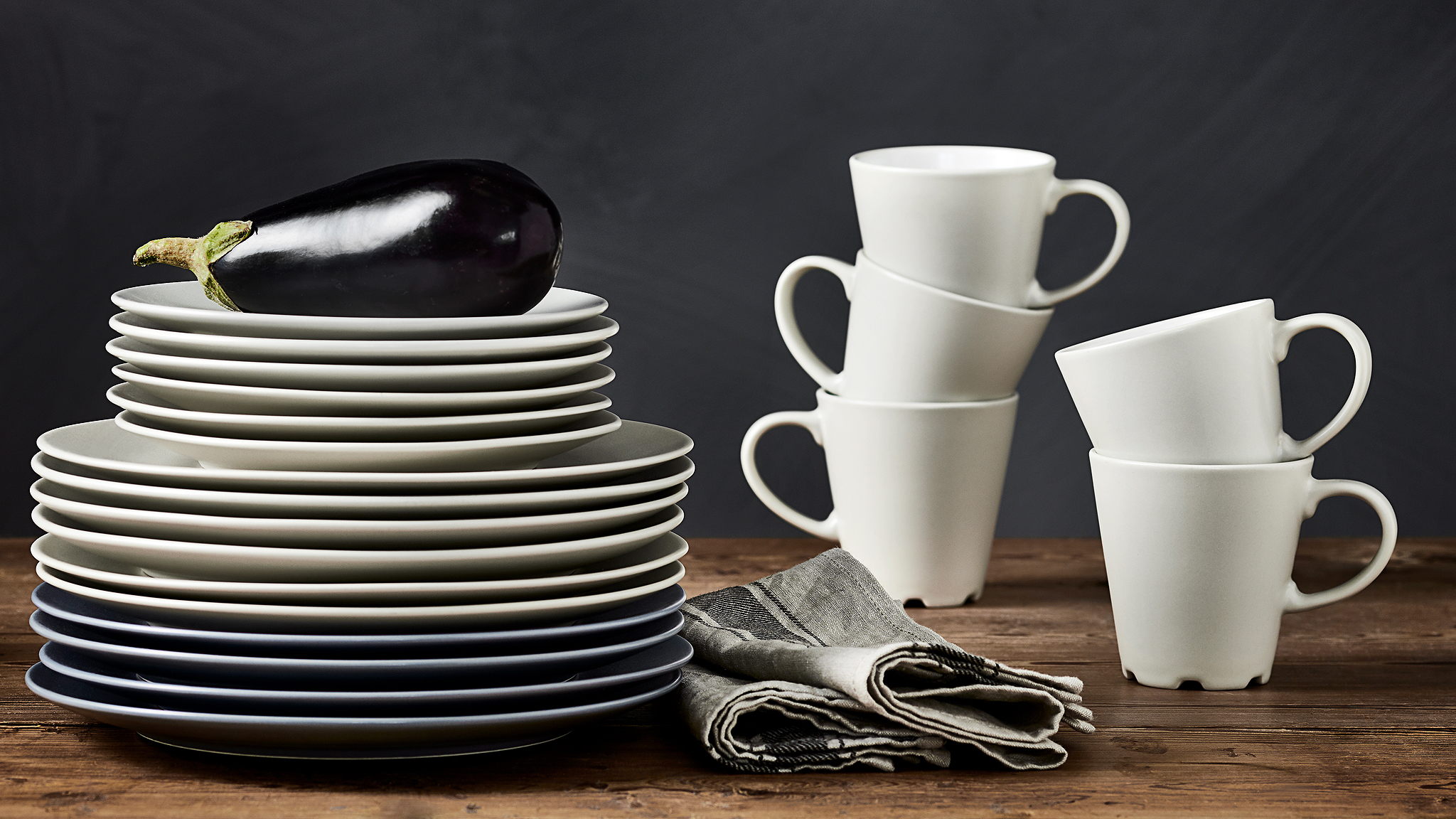 DINERA beige/white mugs are stacked on a worktop next to a stack of beige and grey/blue plates in various sizes.