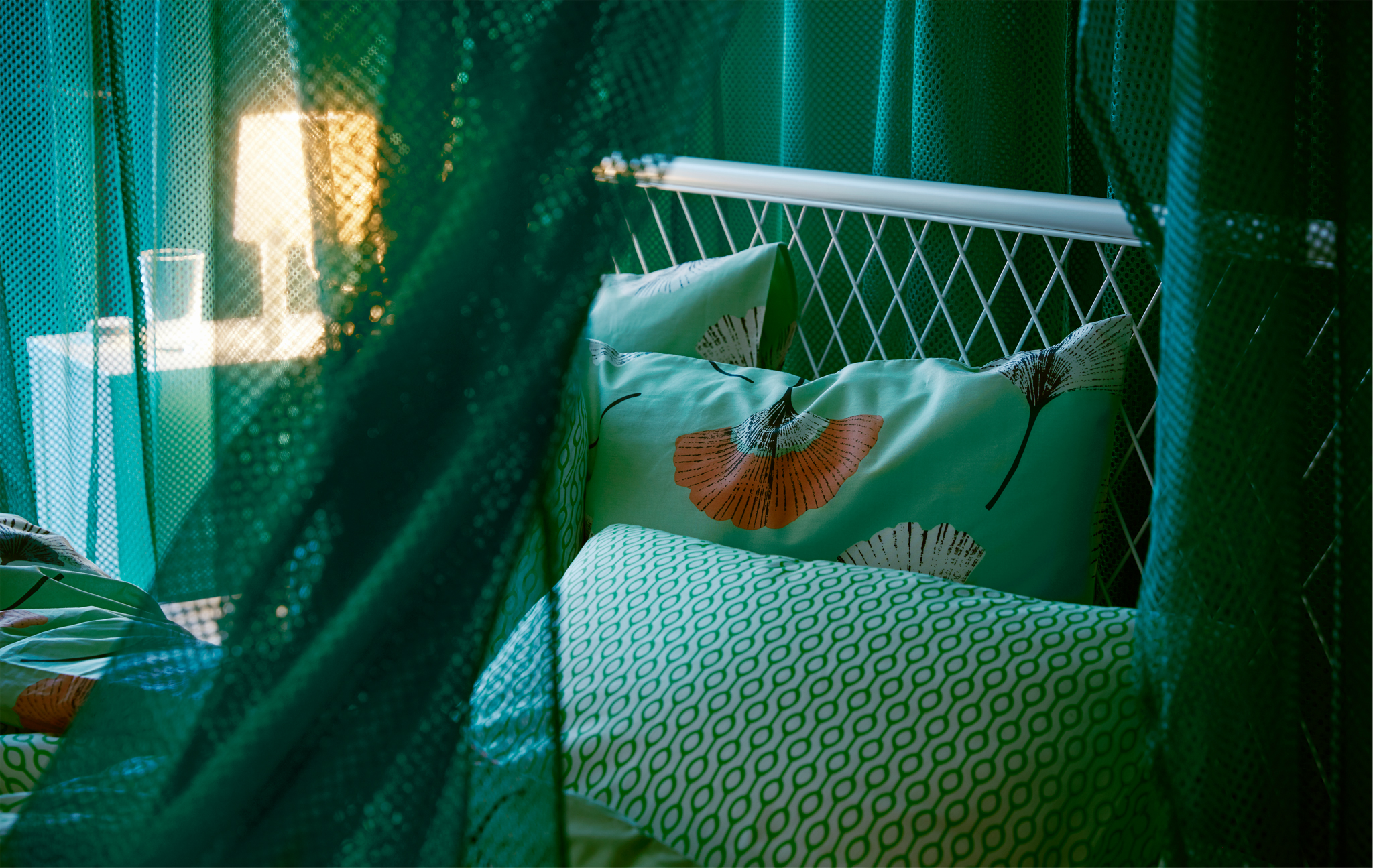 Draped green IKEA GRÅTISTEL net curtains creating a room in the room, while letting through a little light.