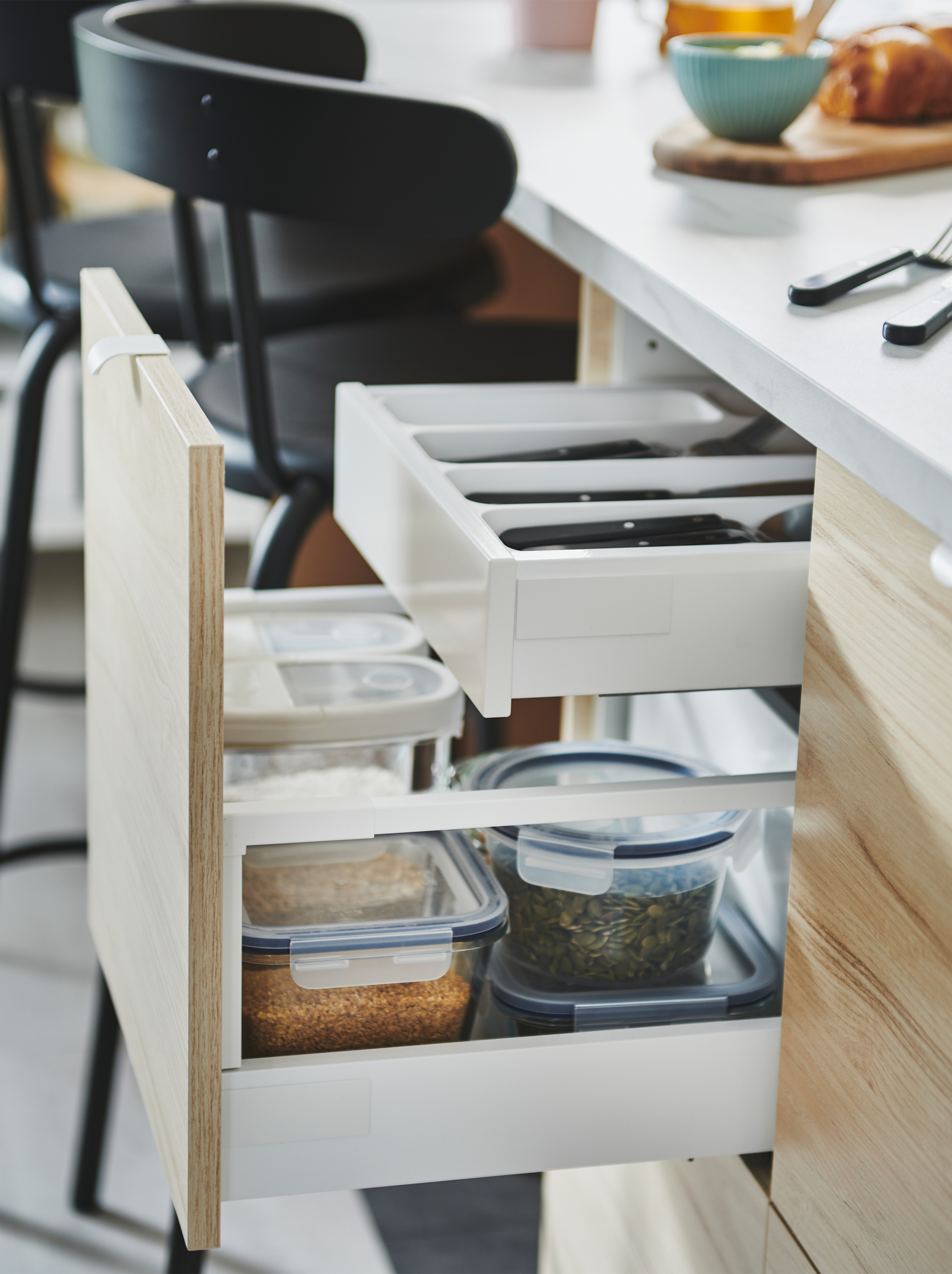 Drawn-out ASKERSUND front of a kitchen island, revealing a two-level drawer solution with both cutlery and food containers.