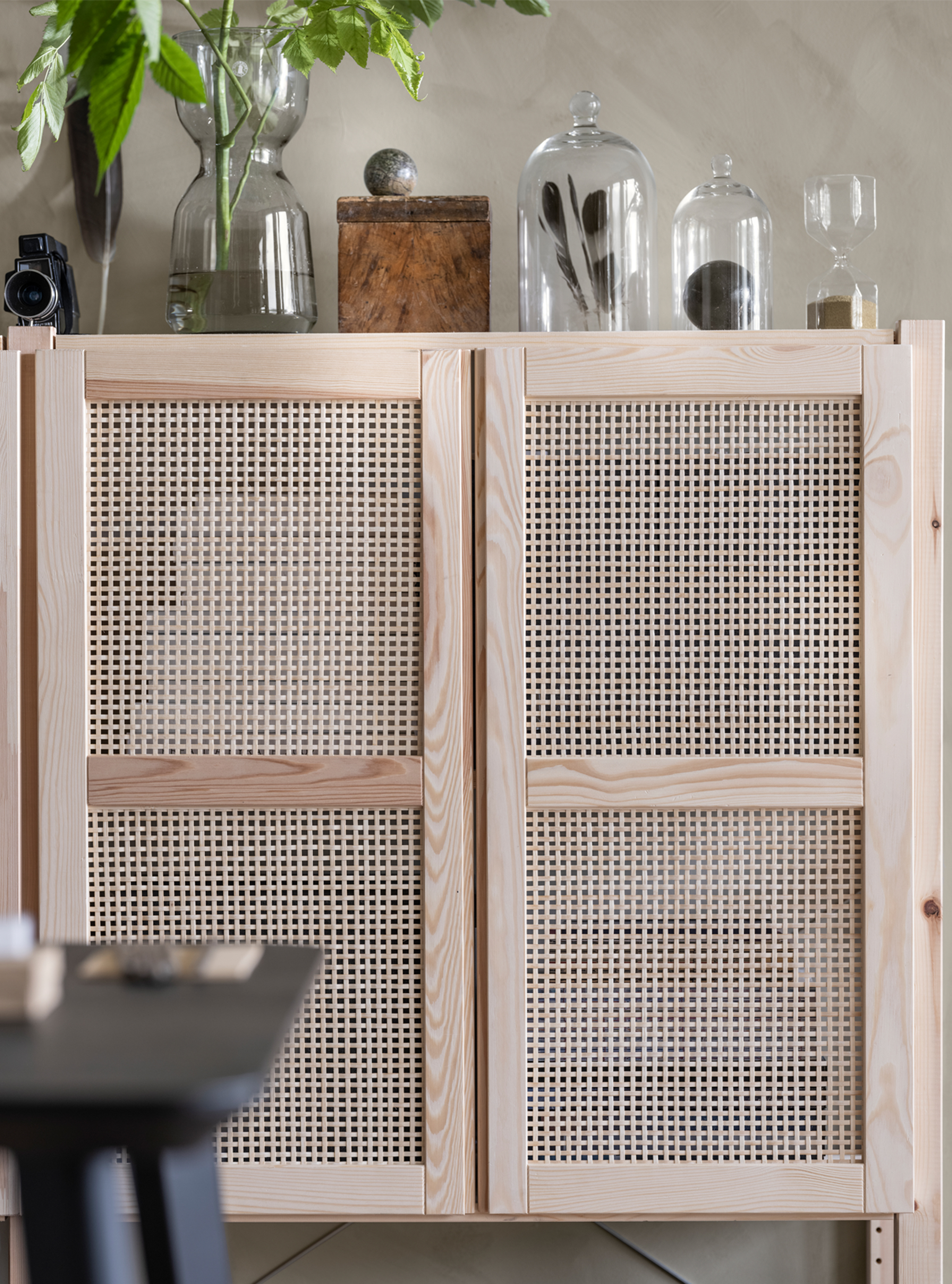 一个带格栅柜门的壁式橱柜上方摆放着玻璃花瓶,瓶中有植物,羽毛和其他