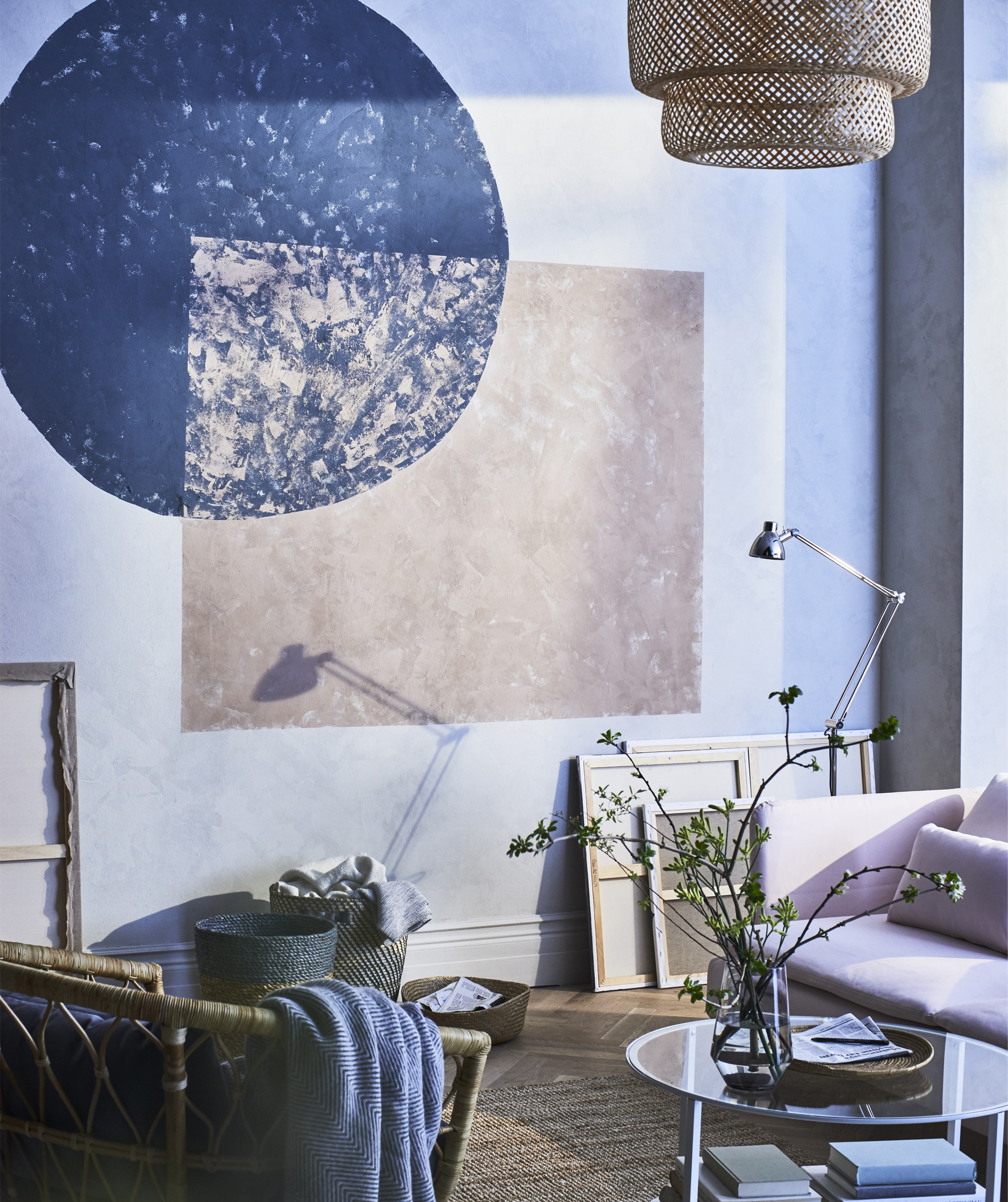 Geometric shapes painted on the wall of a living room in front of a pink sofa and wicker chair.