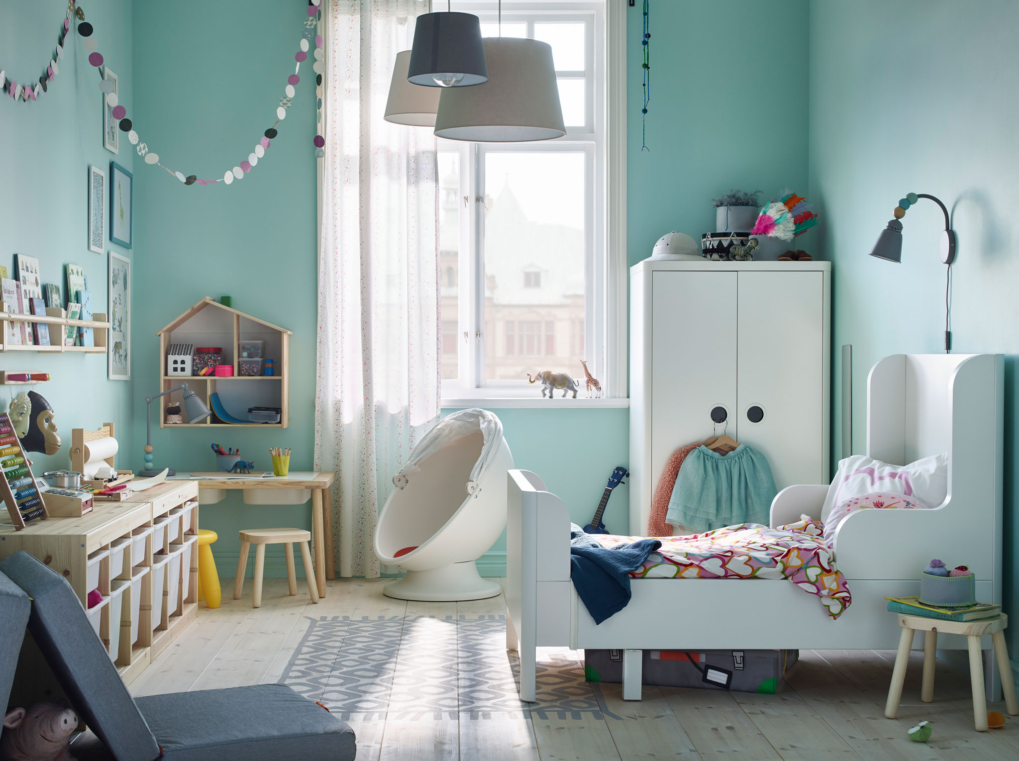 IKEA BUSUNGE white extendable bed and wardrobe along with FLISAT light wood children’s table can transform a room into a playground with safe moving parts.