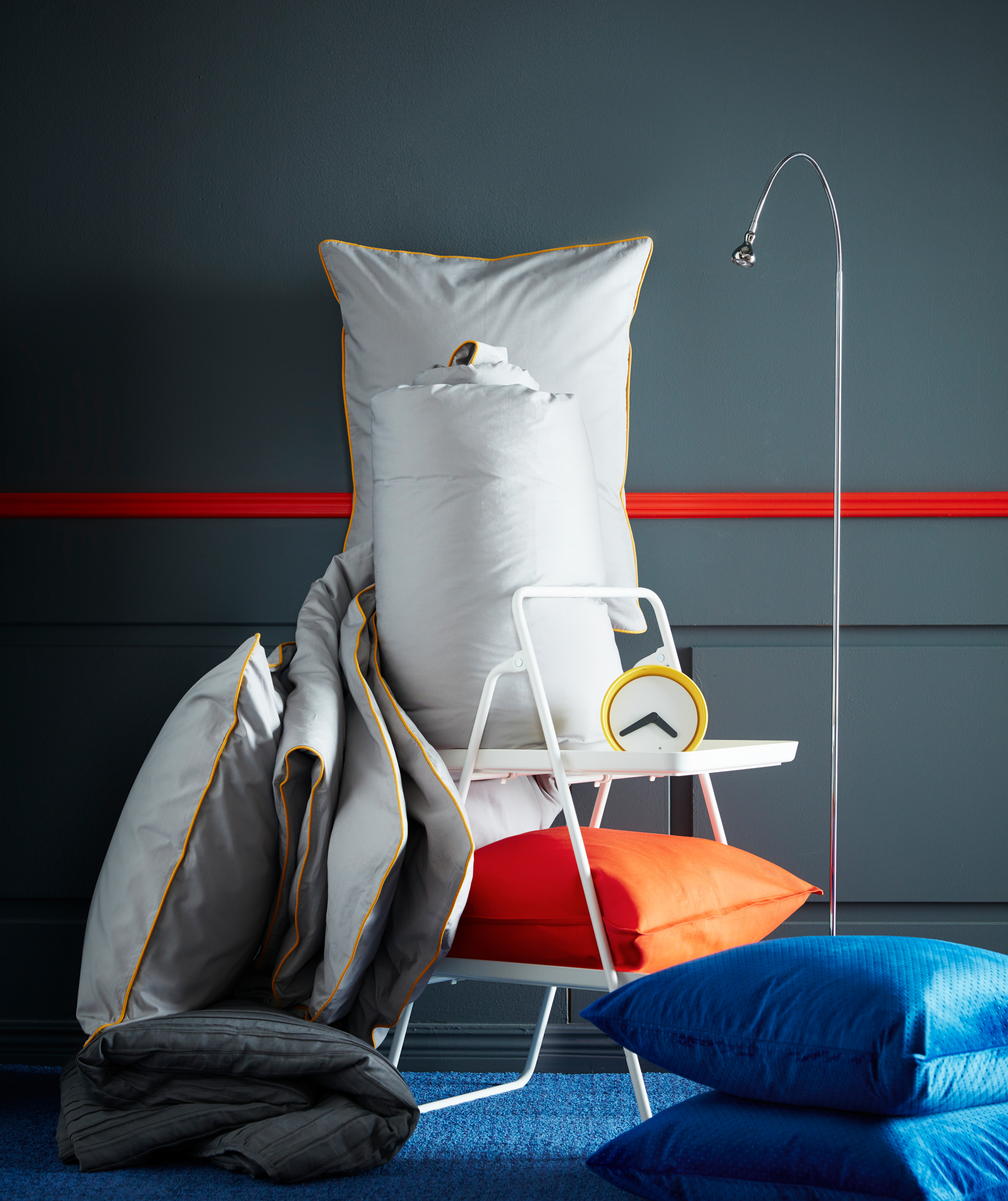 IKEA KUNGSBLOMMA grey quilt cover and pillowcase with yellow rims, an alarm clock, a reading lamp and orange and blue pillows.