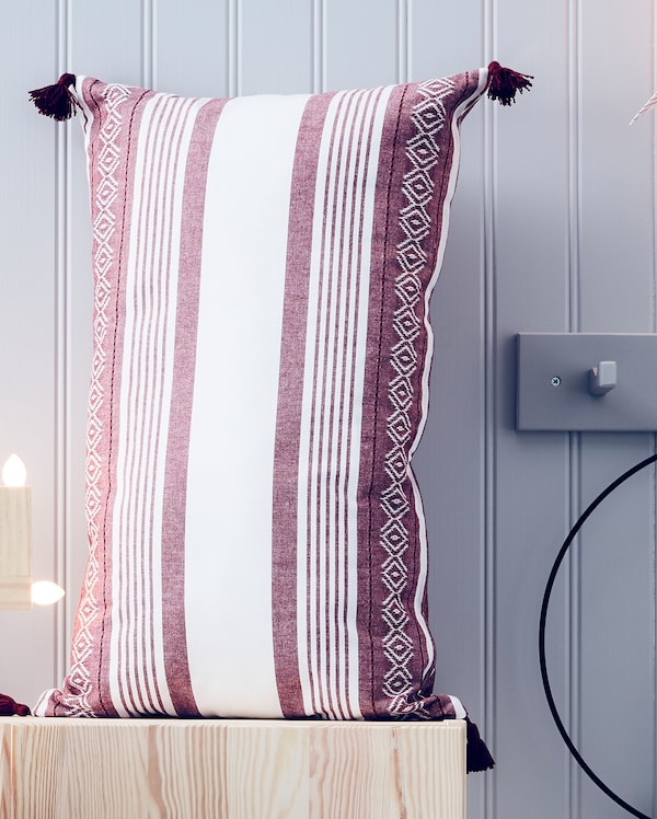 IKEA VINTERFEST pillow case with red and white coloured stripes and other patterns on a wooden bench.