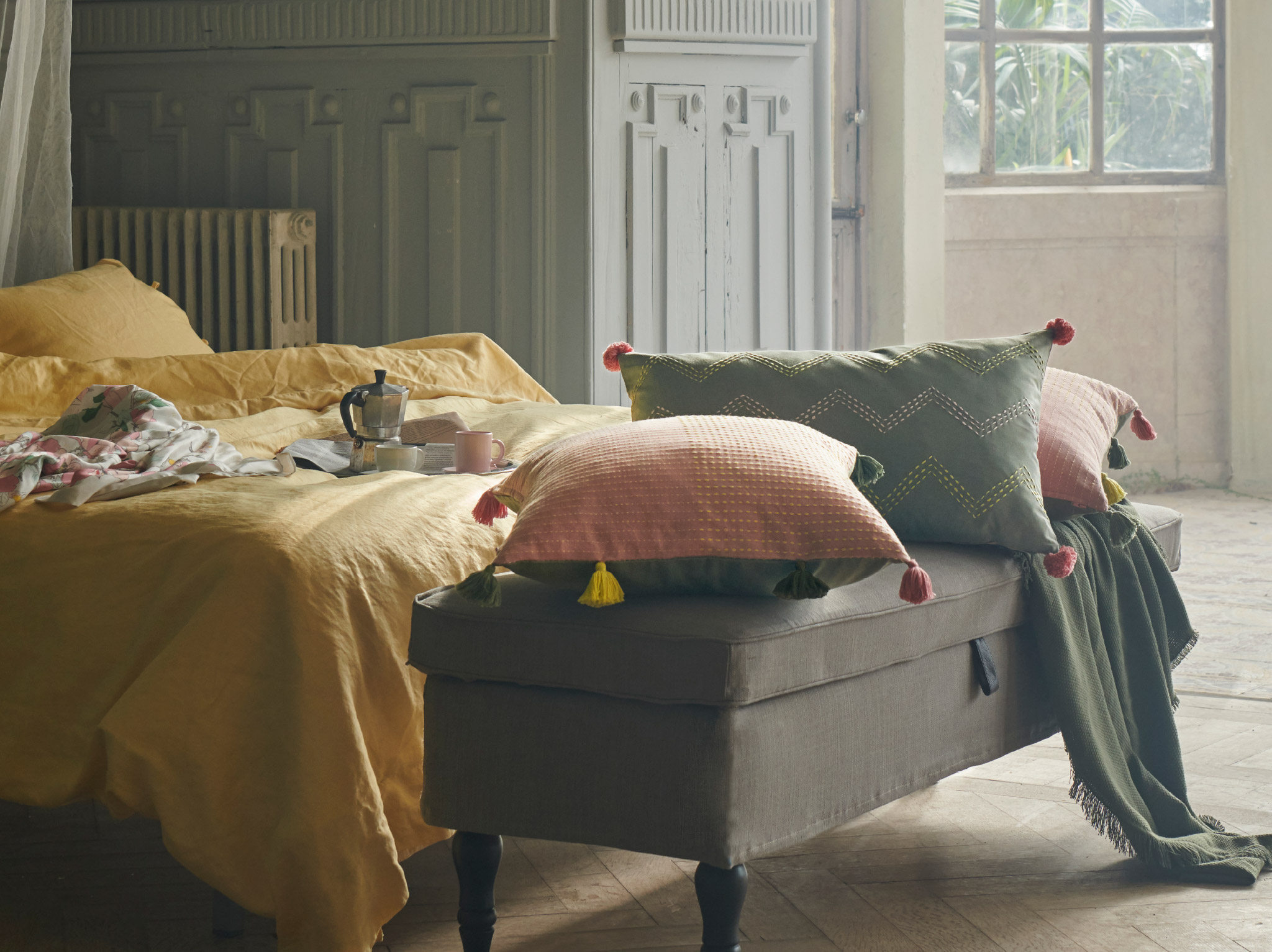 KLARAFINA and MOAKAJSA cushion covers in pink and green are placed on a bench at the end of a bed in a dreamy bedroom.