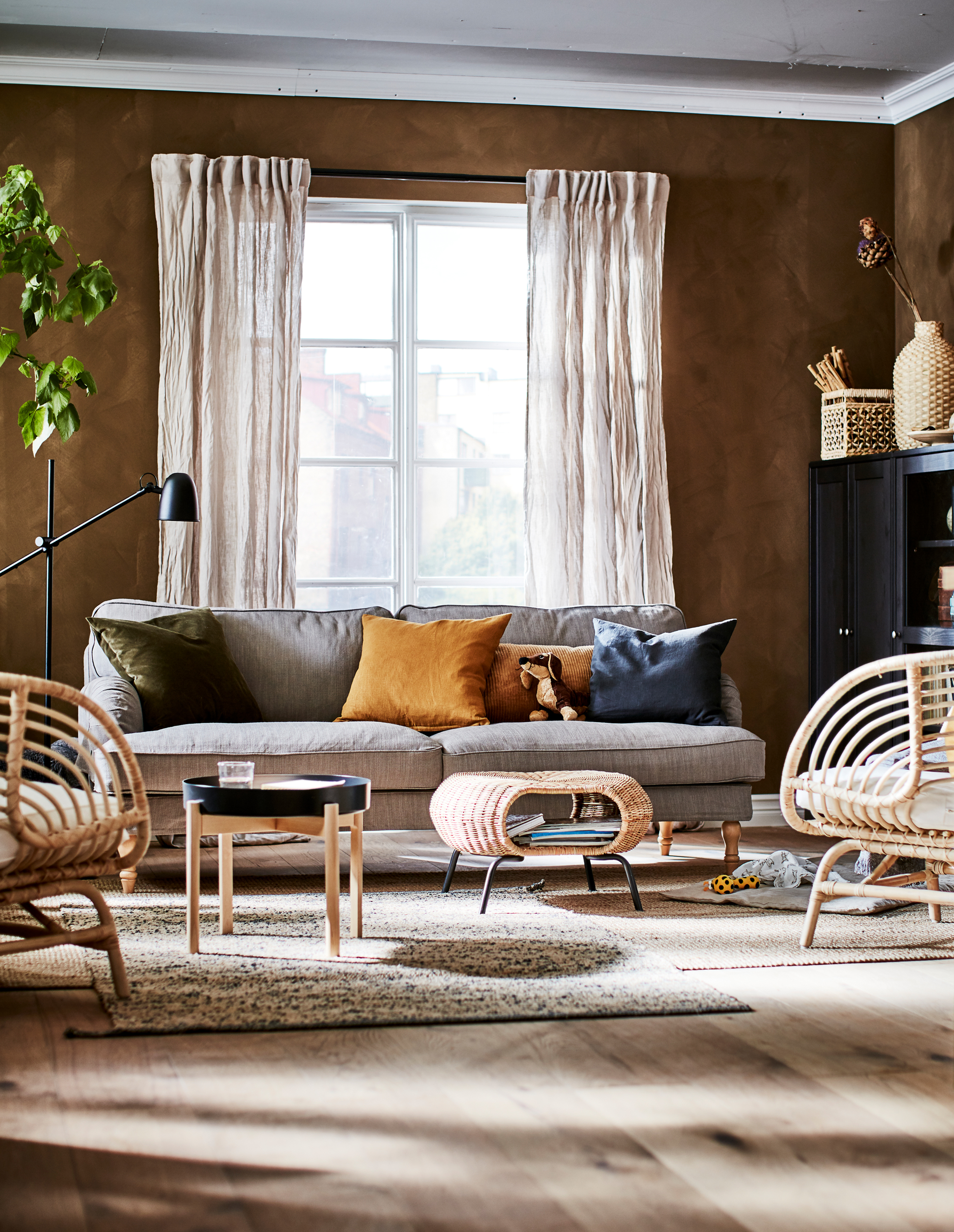 Living room in an earthy-shades colour scheme with decorations, storage, seating, side table, a footstool and a plant.