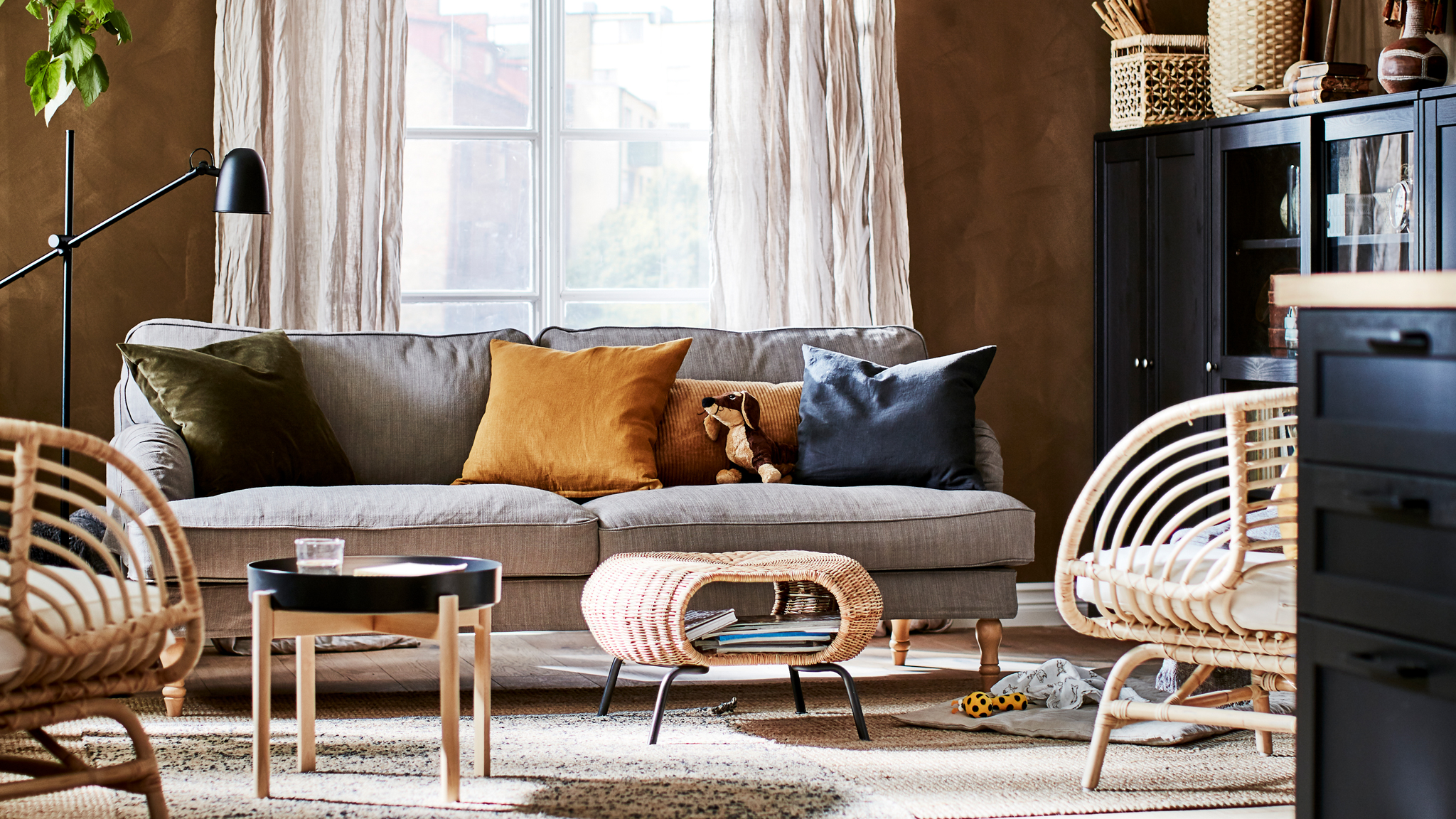 Living room in an earthy-shades colour scheme with decorations, storage, seating, side table, a footstool and a plant.