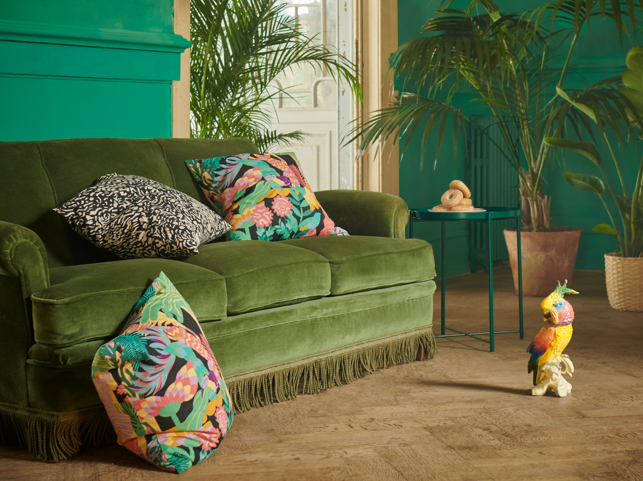 NÄBBFLY and GRIMHILD cushion covers featuring exotic patterns, placed in a green velvet sofa in a grand room with plants.