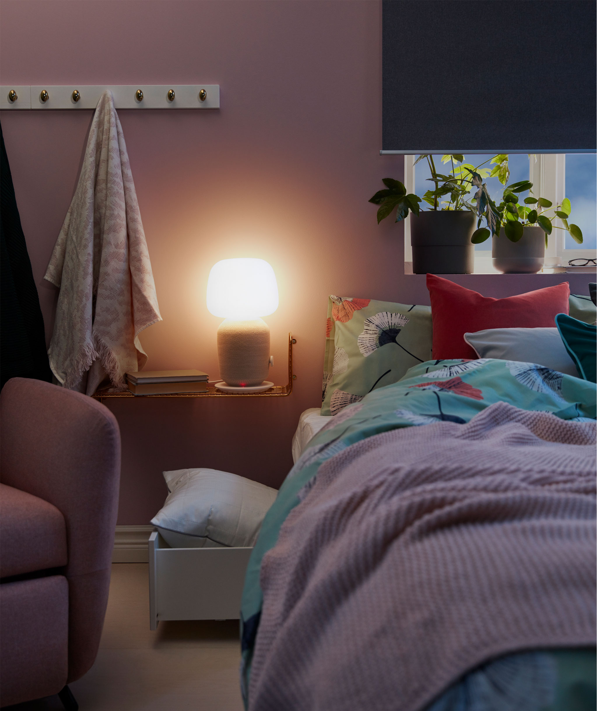 Narrow bedside shelf holding a WiFi speaker table lamp spreading a soft light over a dimly lit bedroom.
