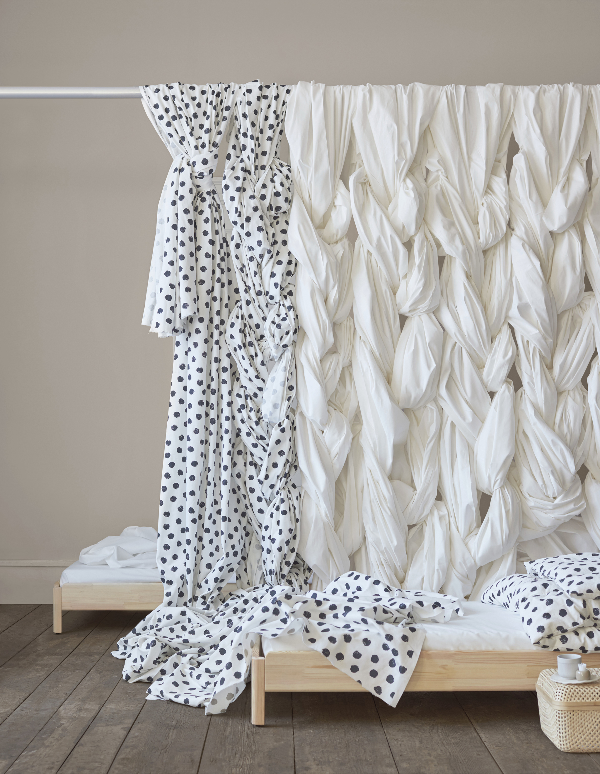 Patterned and plain fabric hanging in plaits over a curtain rod.