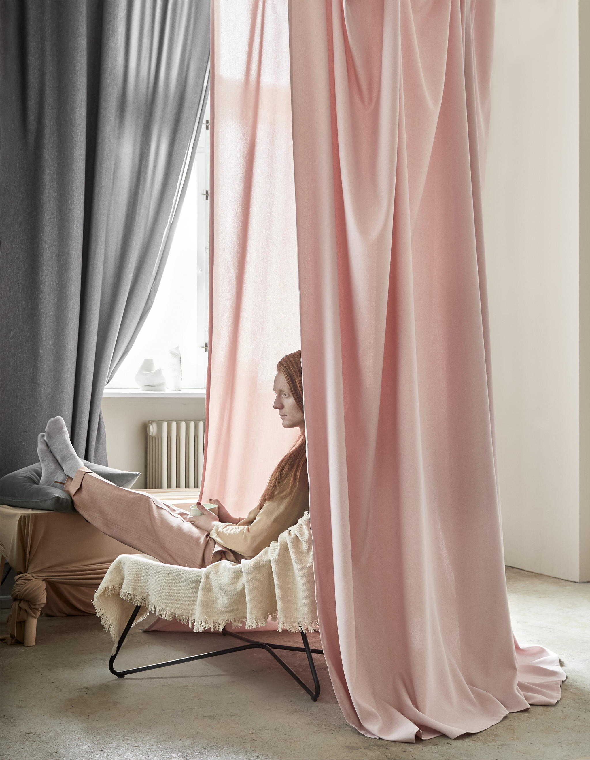 Pink and grey curtains hanging around a man sitting in a chair.