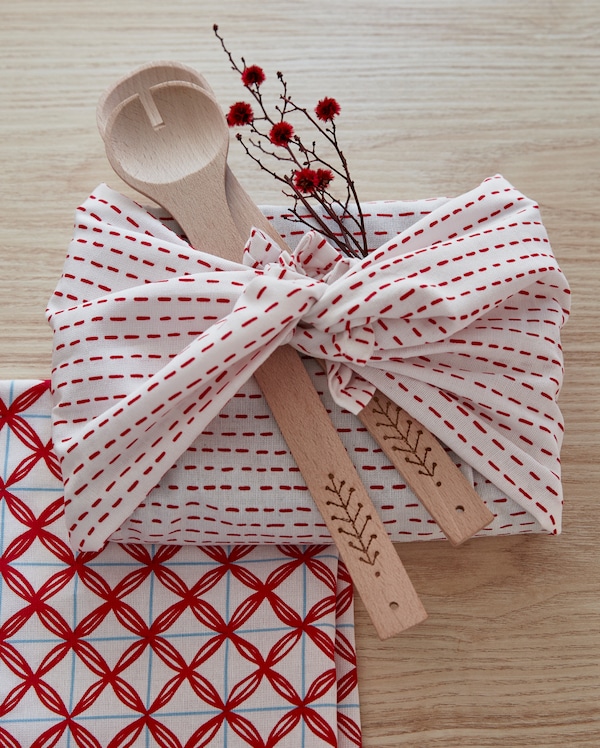 Red and white VINTERFEST kitchen towels wrapped around utensils and a sprig with flowers.