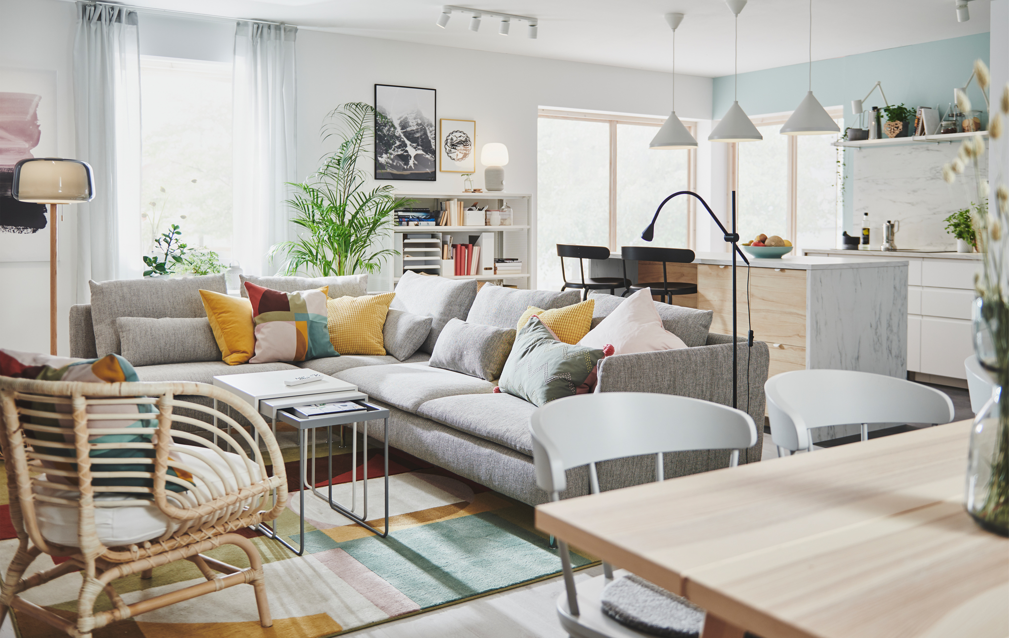Section of a large room with kitchen area with kitchen island, next to a living-room area with large corner sofa.