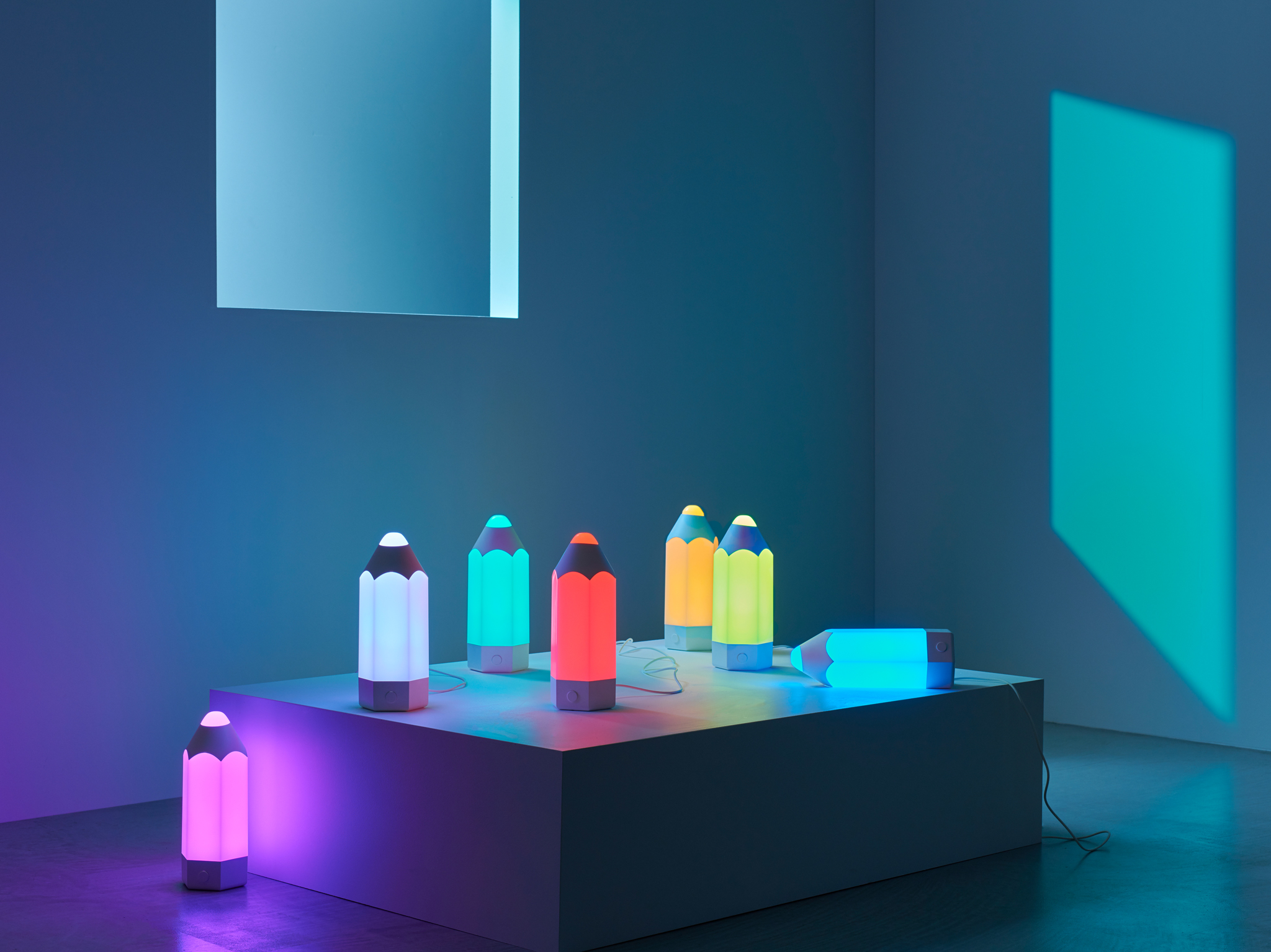 Seven PELARBOJ table lamps with a playful pencil design, showing the seven different colours of light it offers.