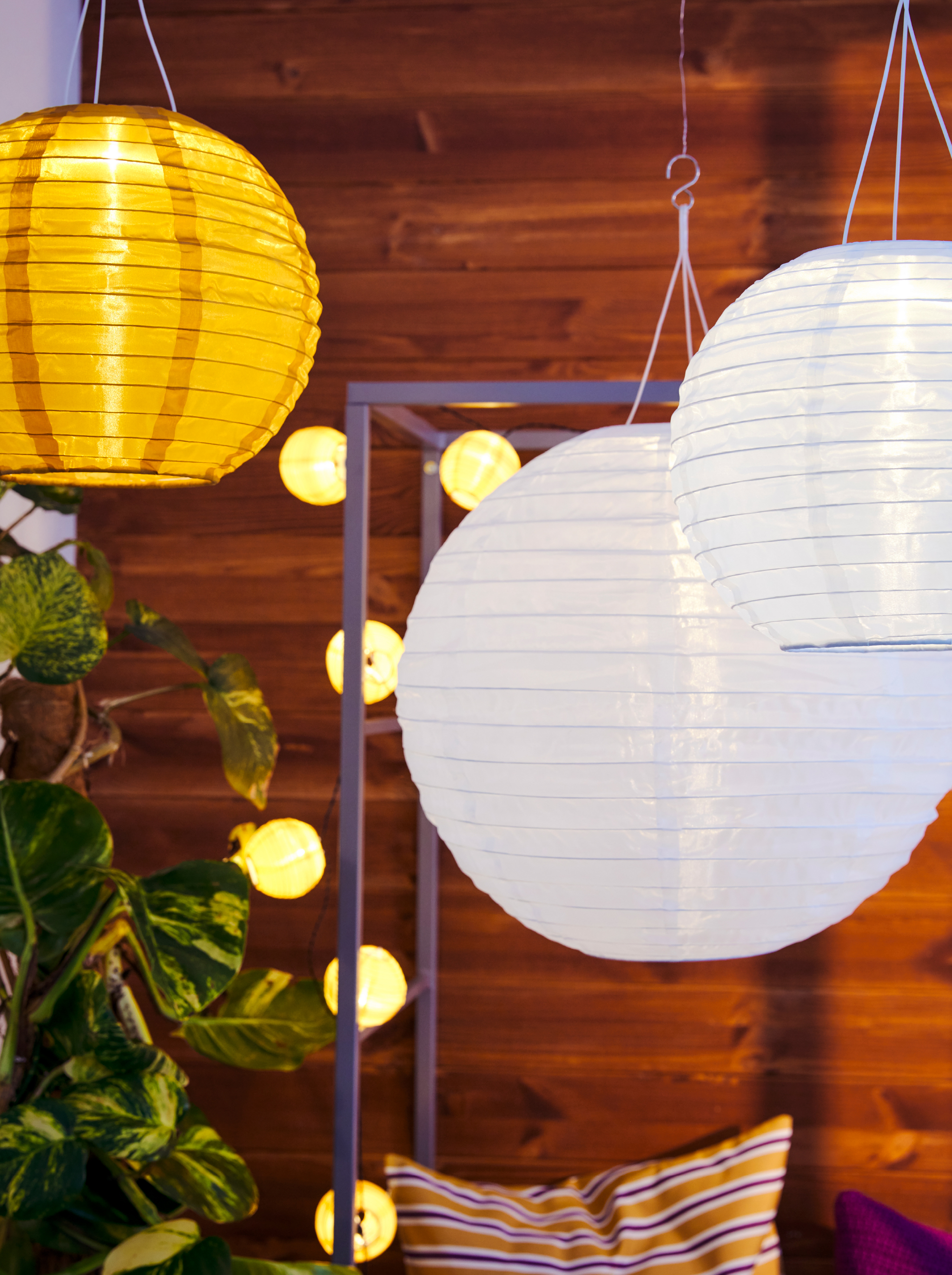 SOLVINDEN solar-powered lamps hang by a SVANÖ arbor bench on a balcony. The bench is decorated with a lighting chain.