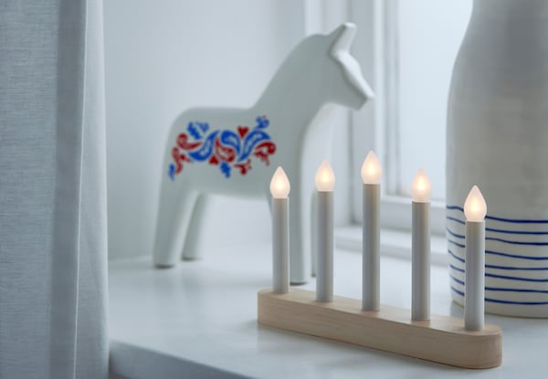STRÅLA candelabra on a window sill with a VINTERFEST horse and white vase with blue stripes.