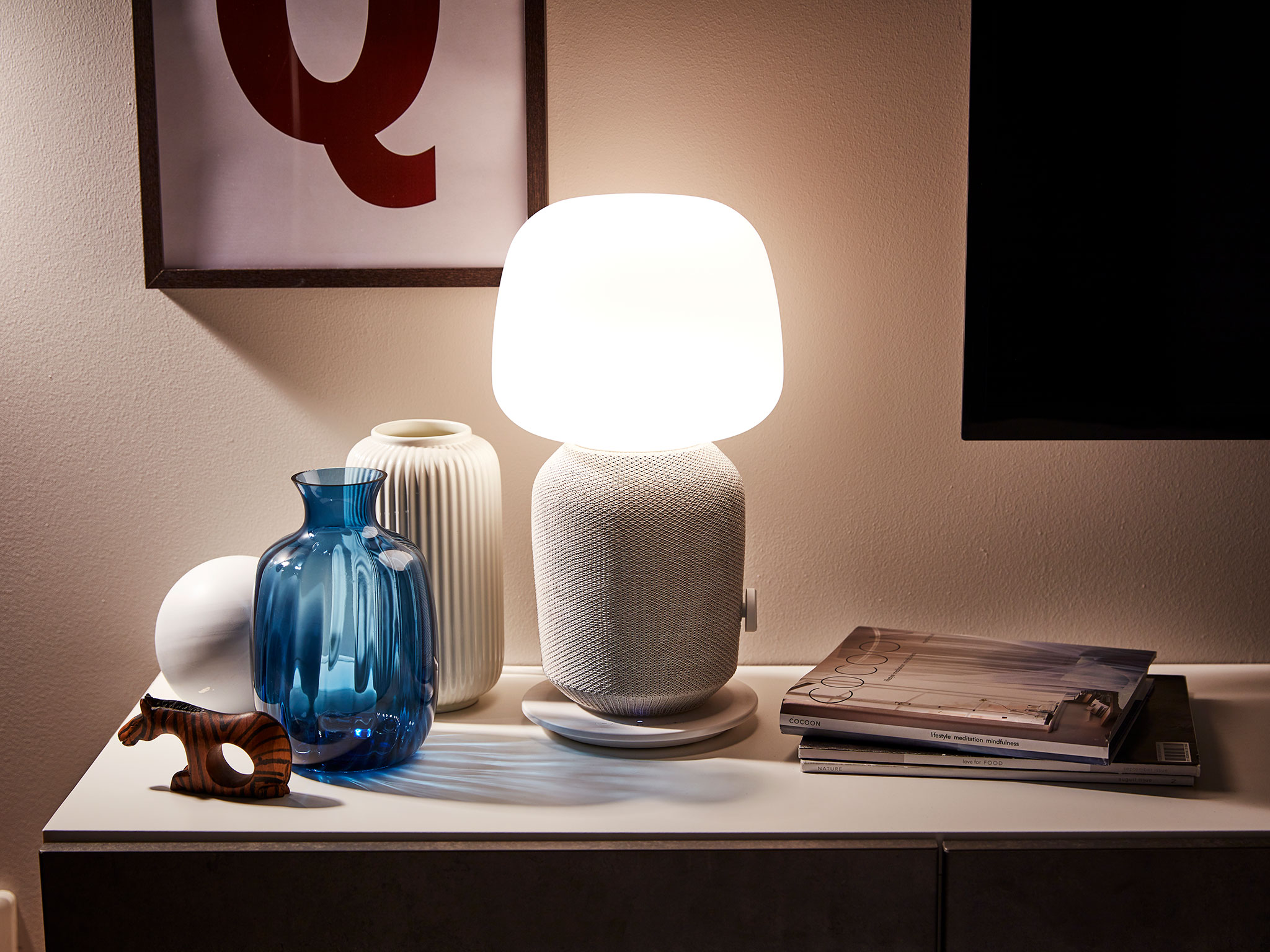 SYMFONISK lamp with WiFi speaker alongside various ornaments and magazines.