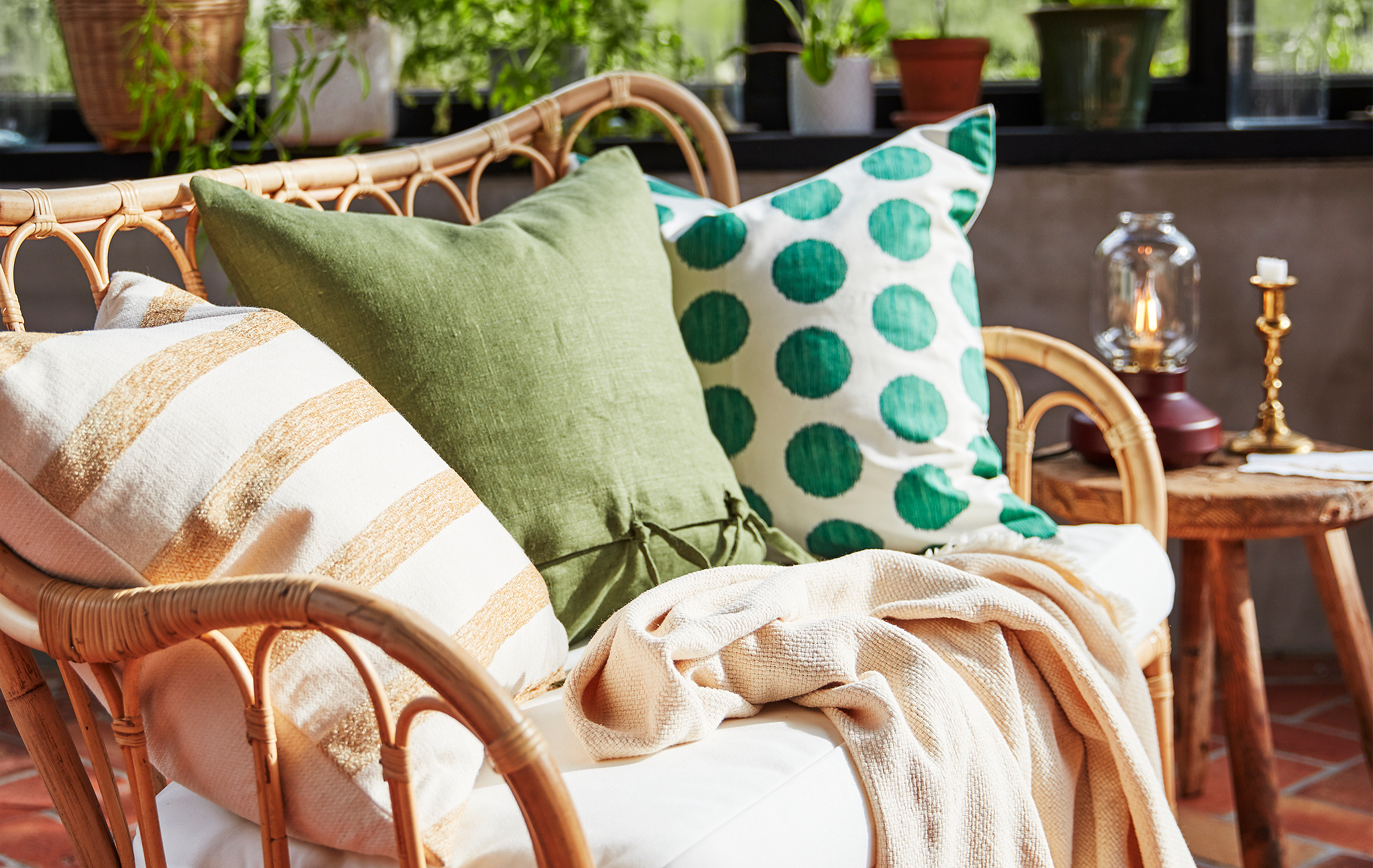 Three pillows in different patterns and muted colours, shown in a sofa of natural rattan in a living room.