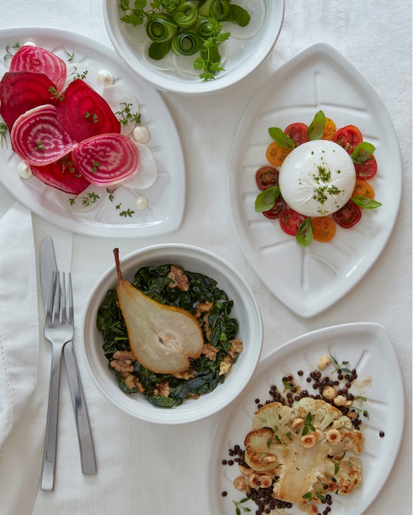 Three white leaf-shaped VINTERFEST plates and two round bowls with savouries on a white tablecloth.