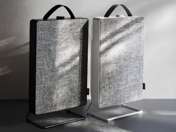 Two FÖRNUFTIG air purifiers in black and white with a grey side standing next to each other in a simple grey setting.