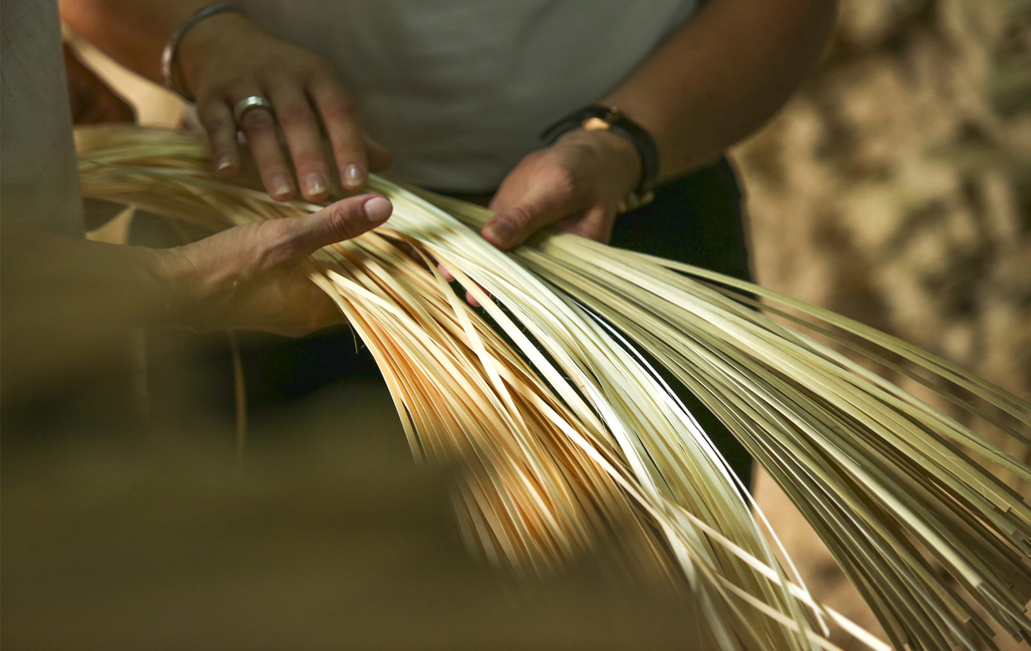 Two people holding strips of raw bamboo.