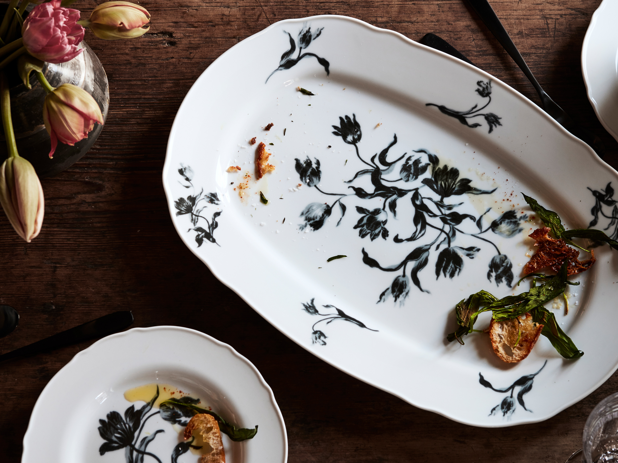 UPPLAGA serving plate and side plate with a rustic floral pattern on white placed on a wooden table with tulips.